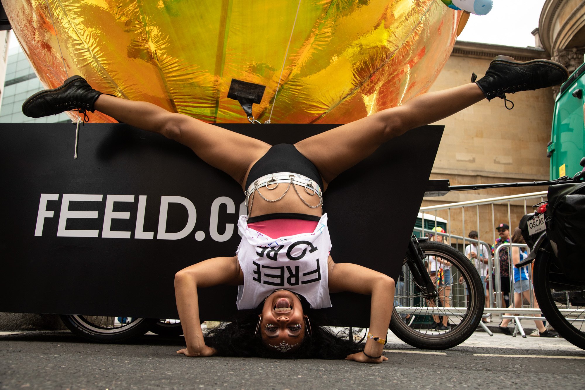 A Pride participant performing a headstand beside a Feeld float and a large gold balloon.