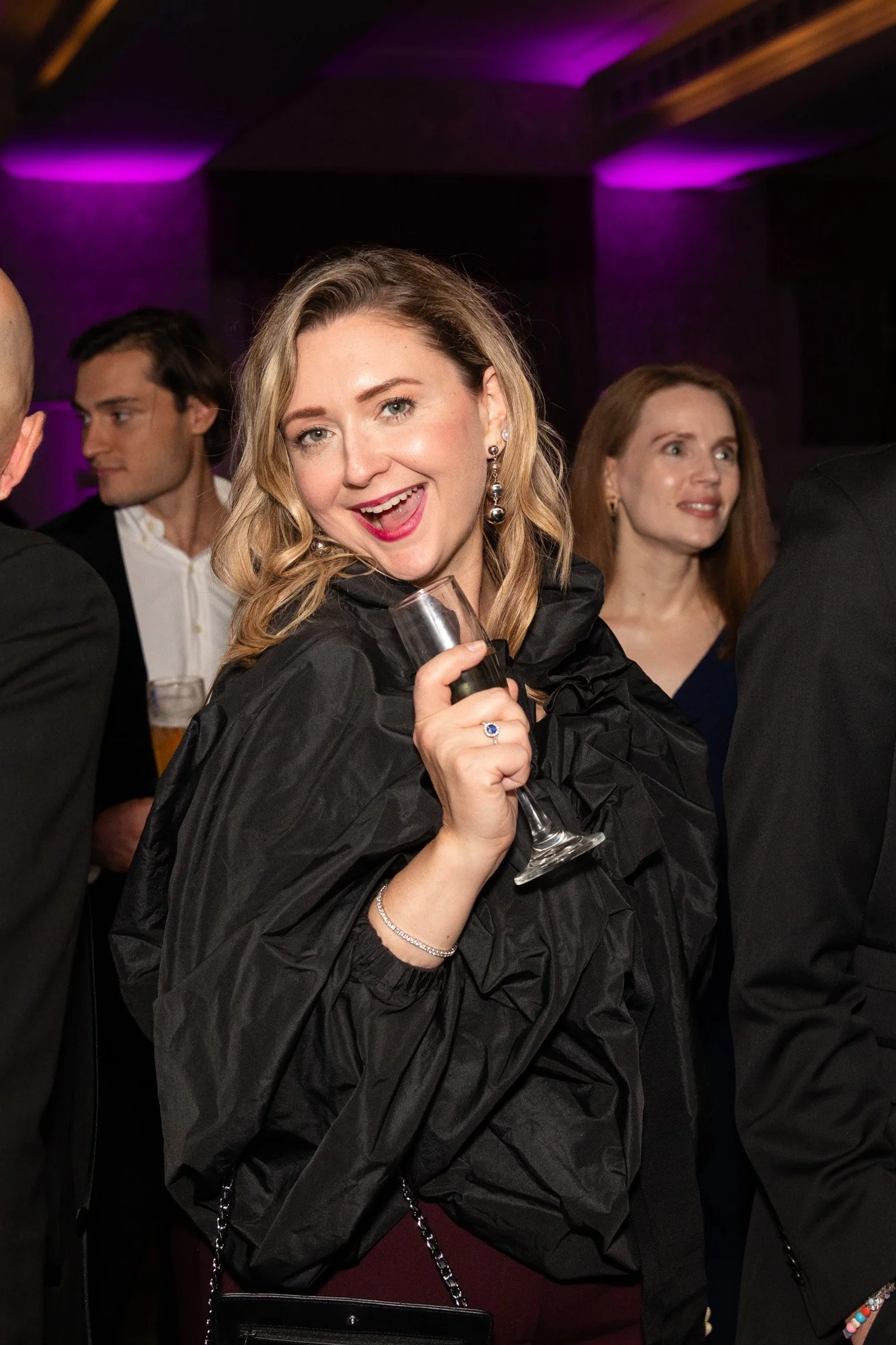 A smiling guest holding a champagne flute at a reception lit in purple.