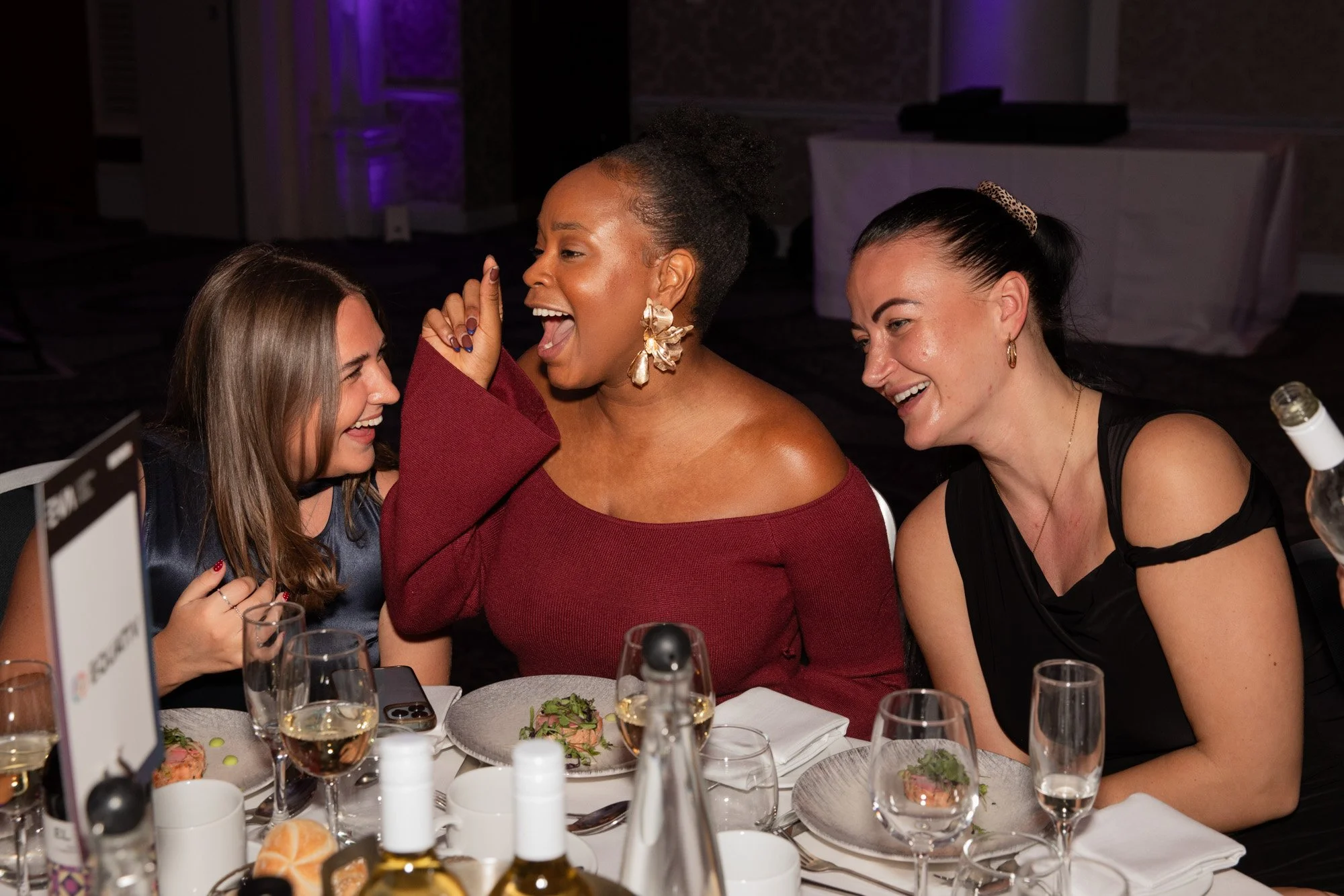 Three guests laughing and chatting around a table at an awards dinner.