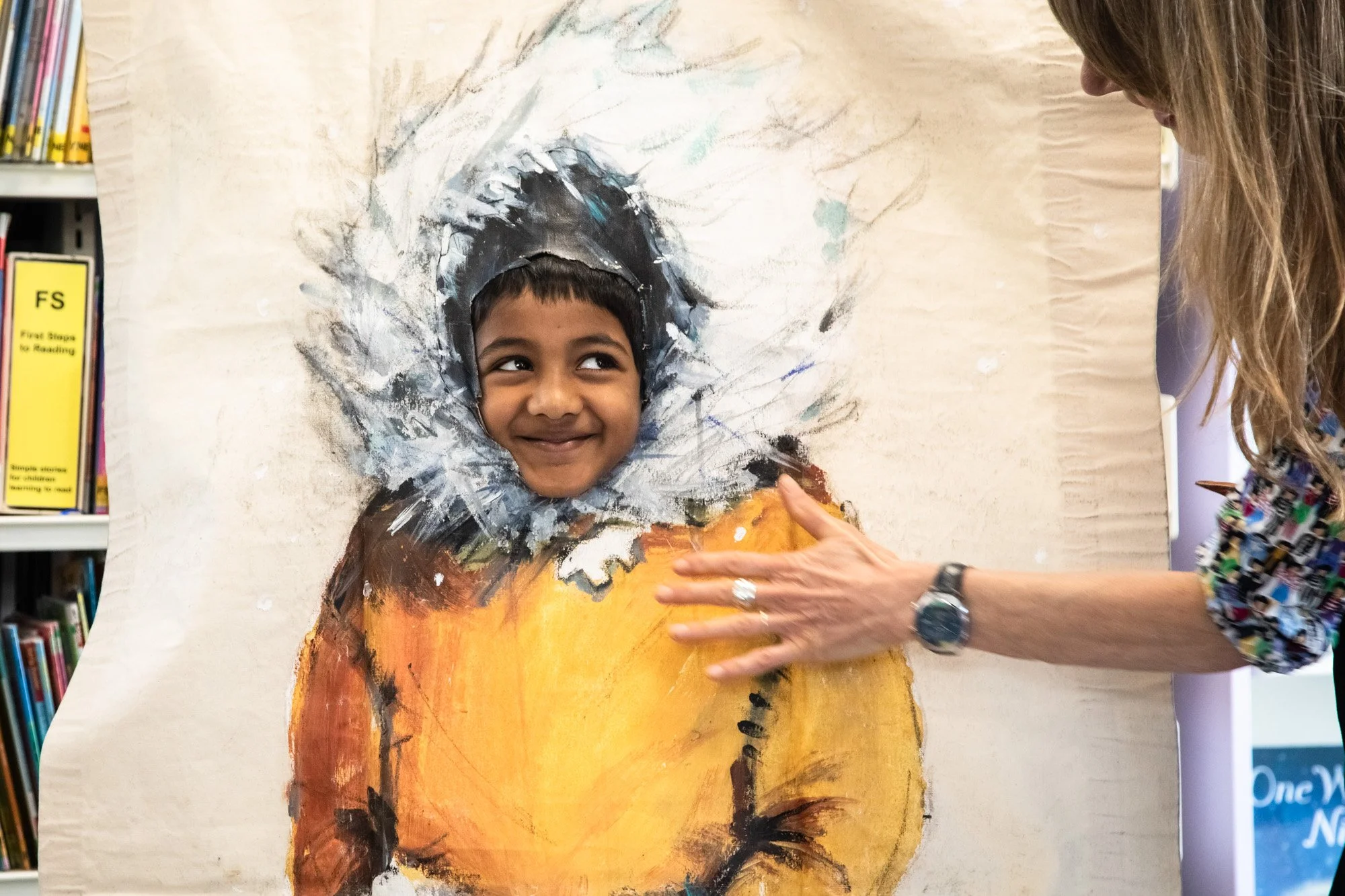 A smiling child looking through a painted character cutout during a picture-book activity.