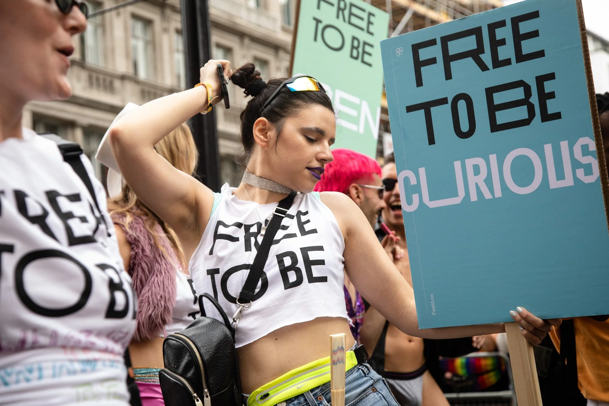 A participant raising an arm during the Feeld Pride parade beside a blue sign reading “Free to be curious”.
