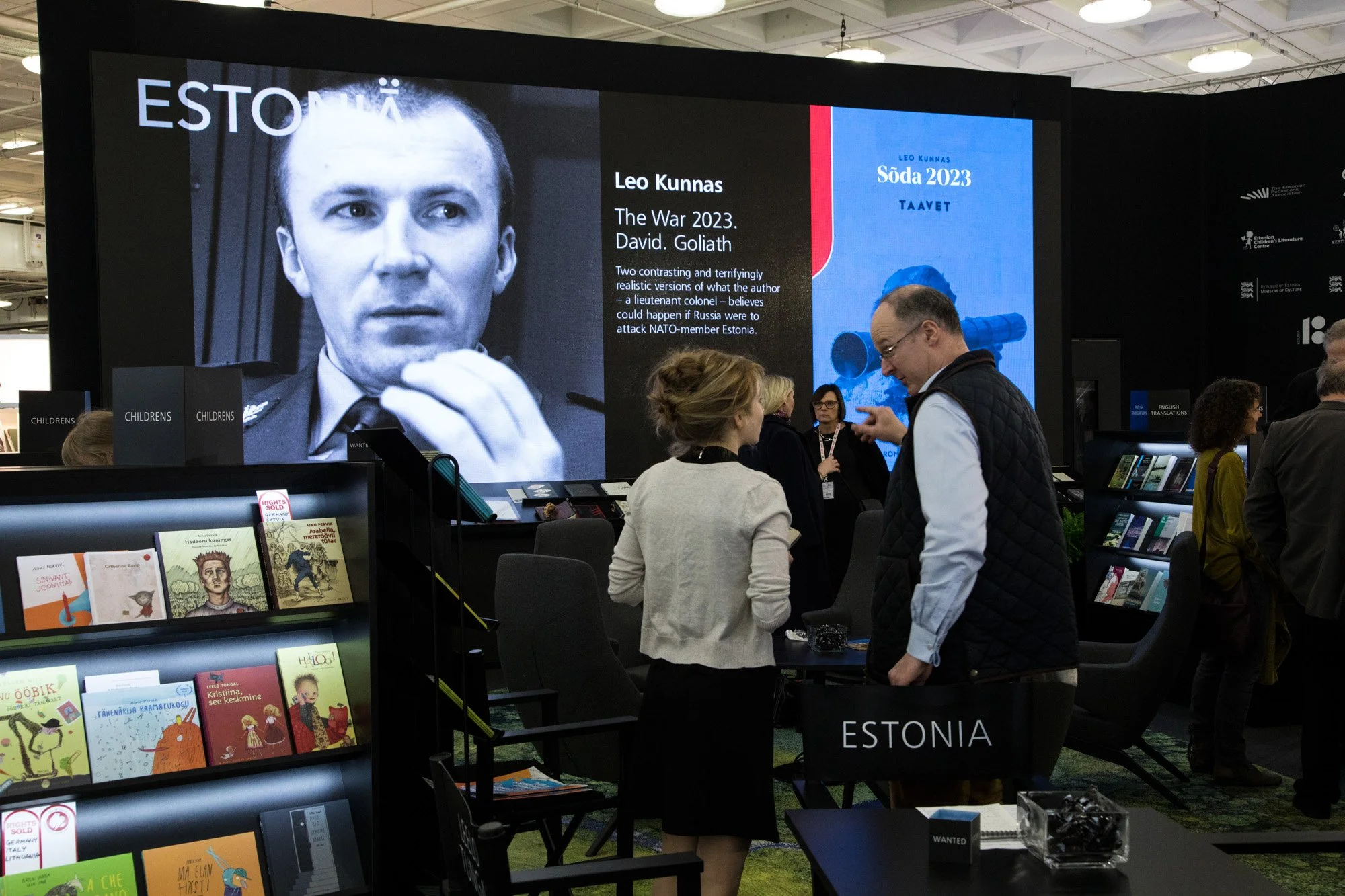 Visitors browsing books and talking at the Estonia exhibition stand at a book fair.