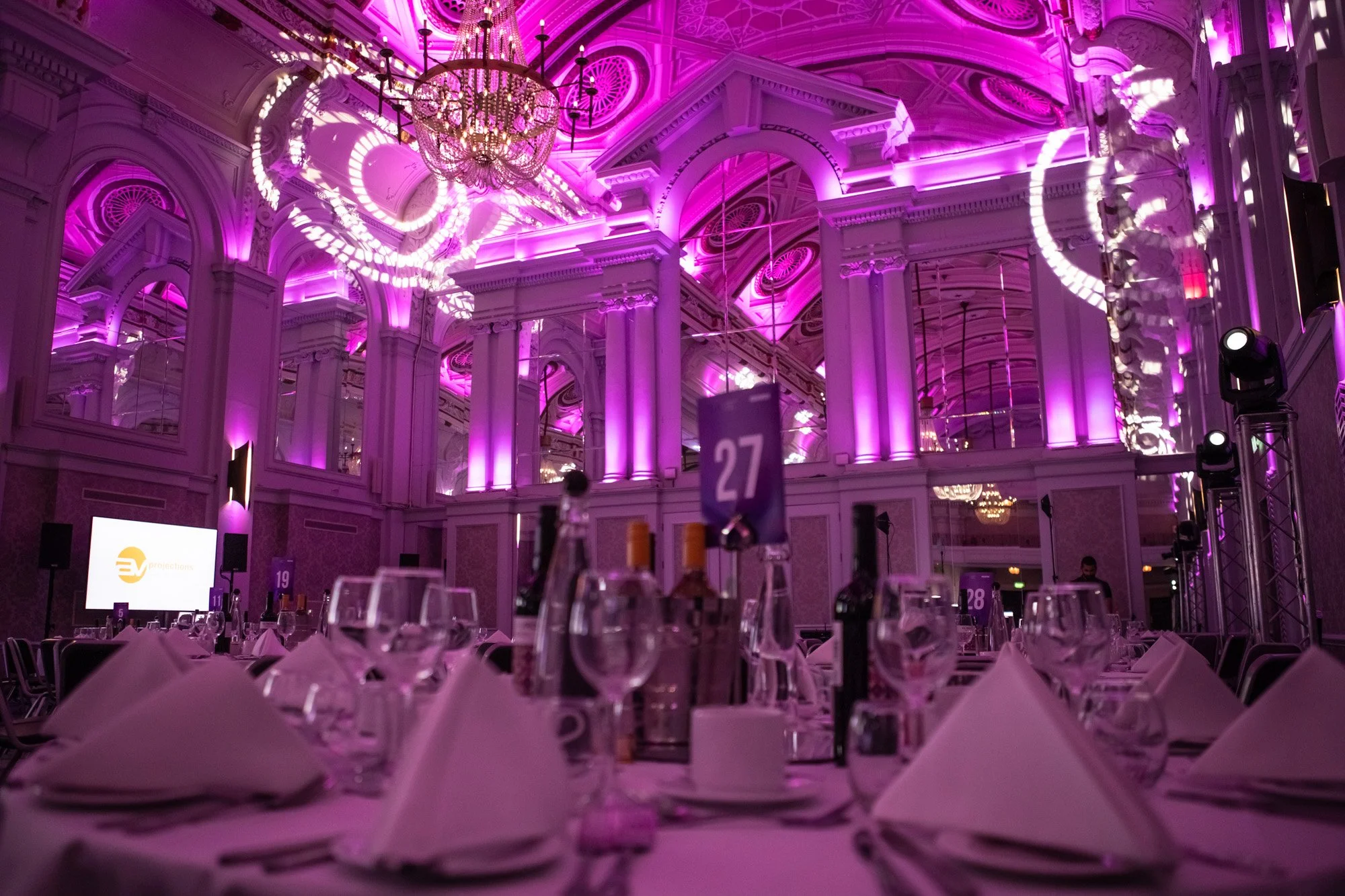 An ornate banquet hall set for an awards dinner and illuminated in purple.