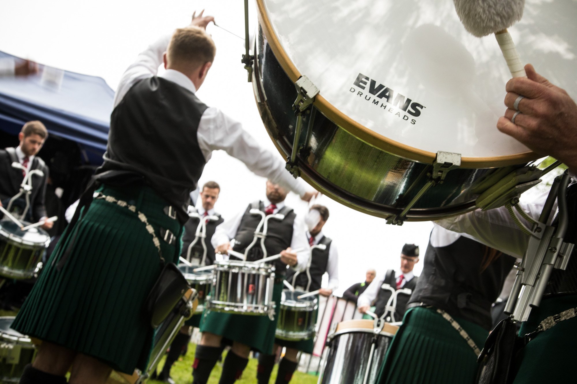 A bass drum and musicians in green tartan kilts during an outdoor pipe-band performance.
