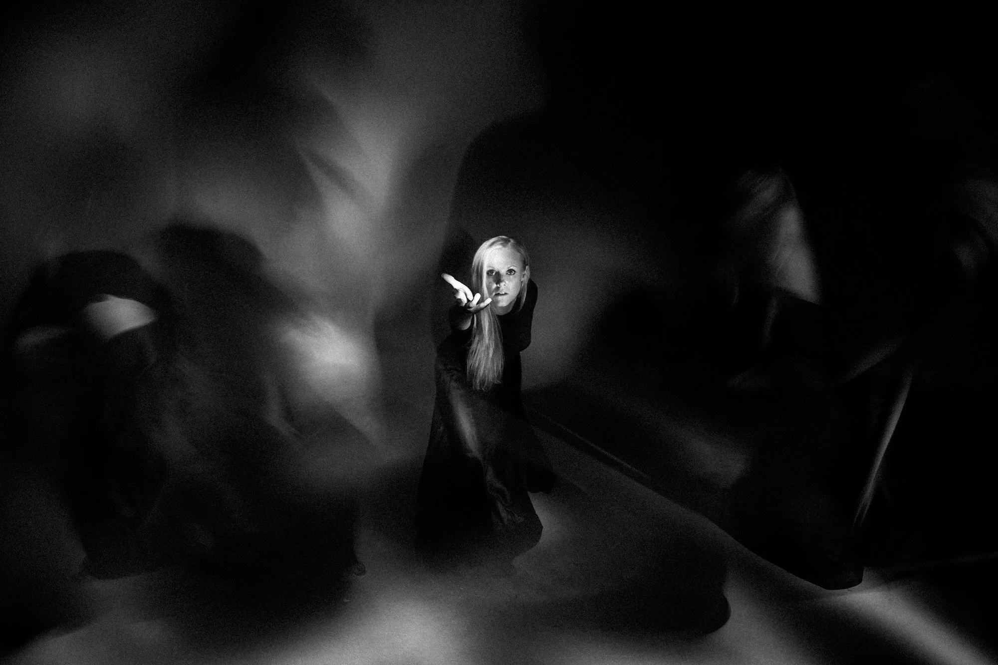 Black-and-white photograph of a performer reaching towards the camera amid blurred shapes.