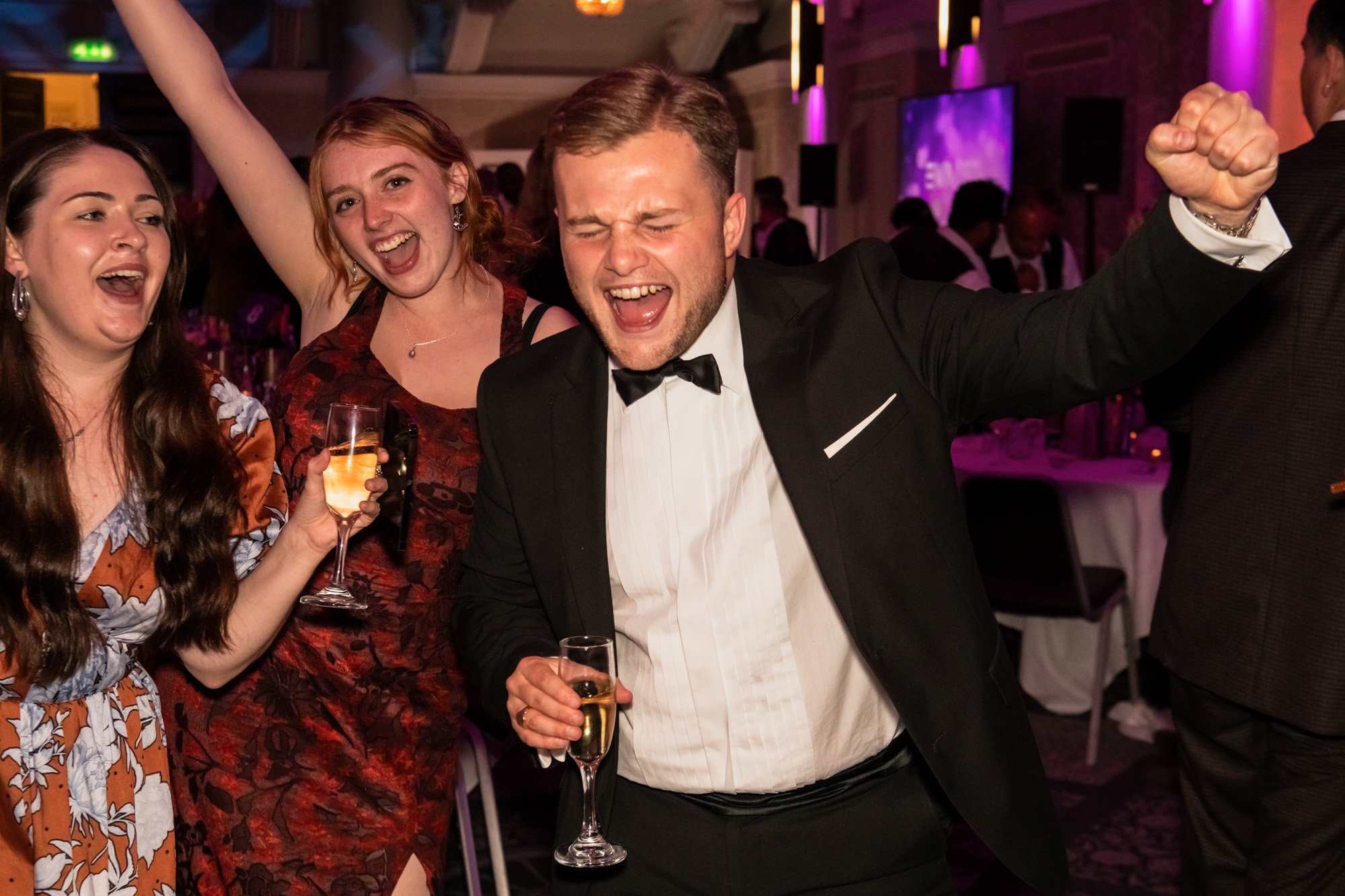 Guests cheering with raised arms and drinks at an awards celebration.
