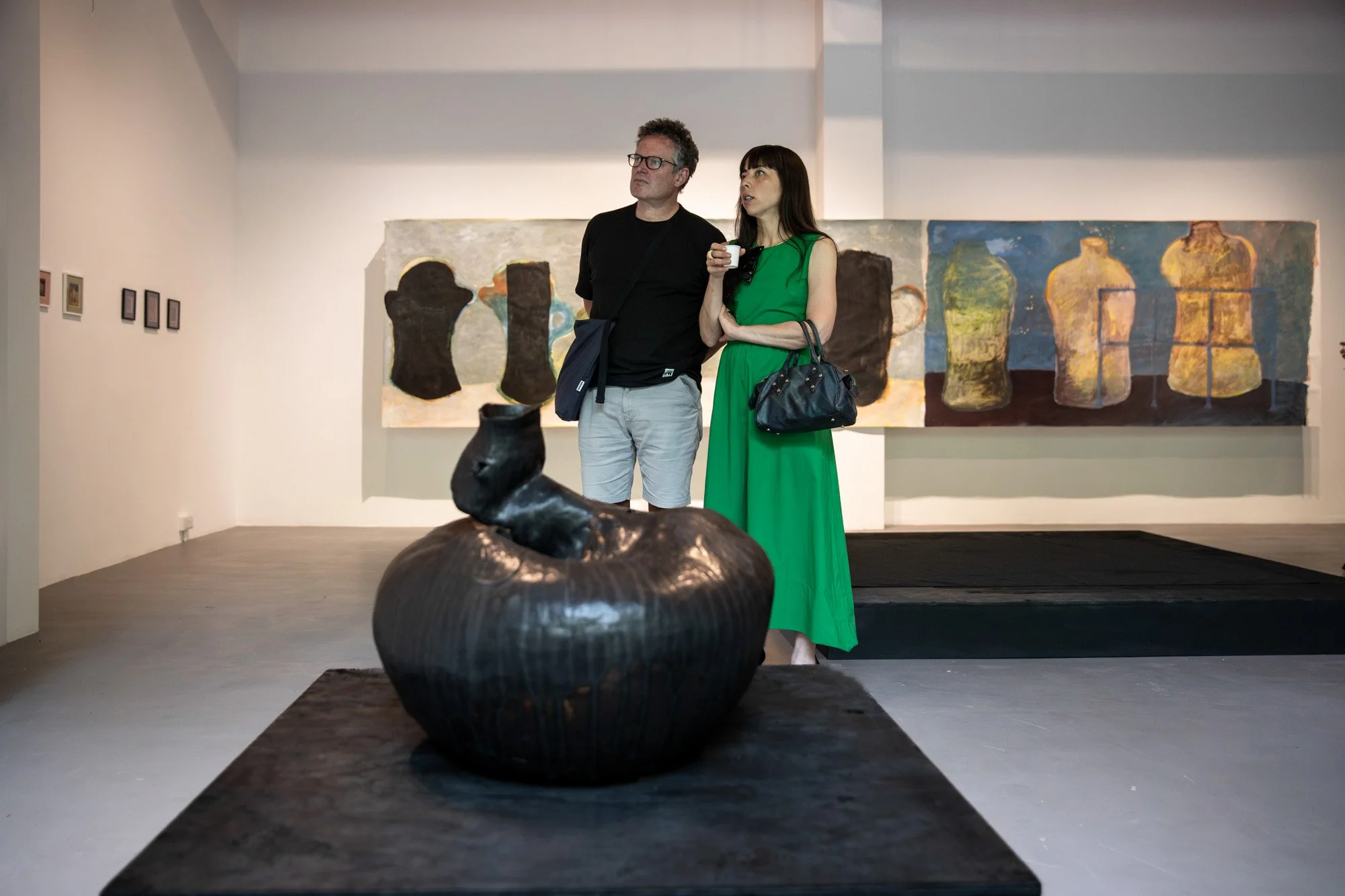 Two visitors standing beside a large sculpture and paintings at the Locus of Voices exhibition.