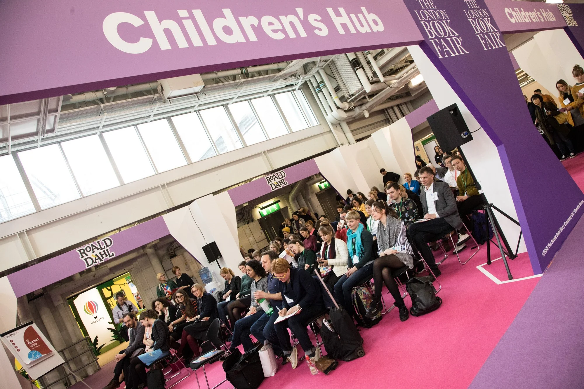 An audience seated beneath the Children's Hub sign at a book fair.