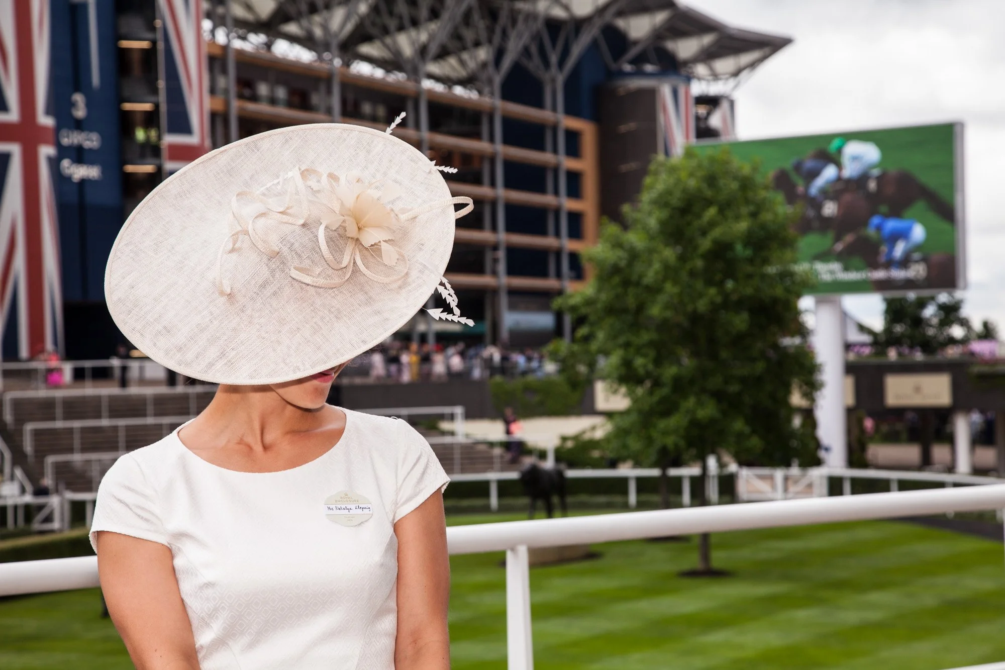 A guest in a large cream hat beside the racecourse at Royal Ascot.