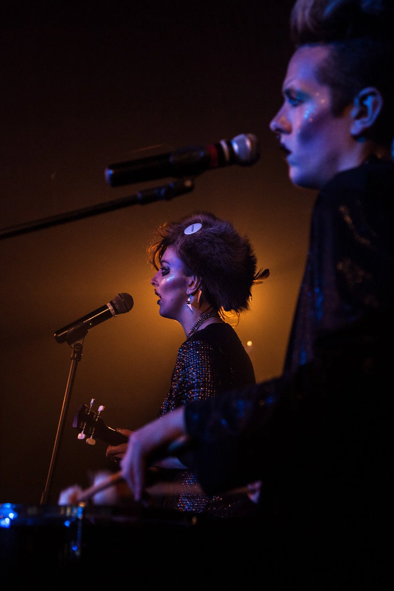 A performer singing into a microphone under warm and purple stage lighting.