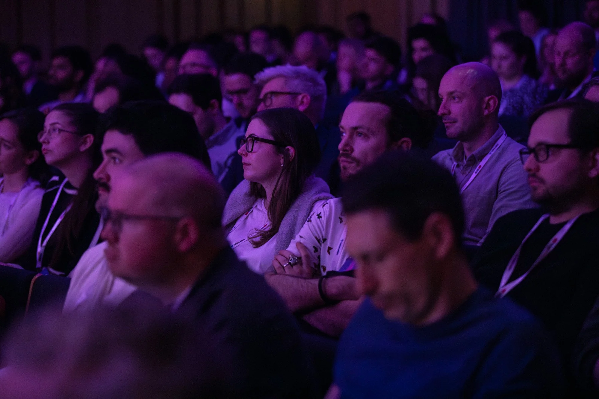 Rows of delegates watching a conference presentation under purple stage lighting.
