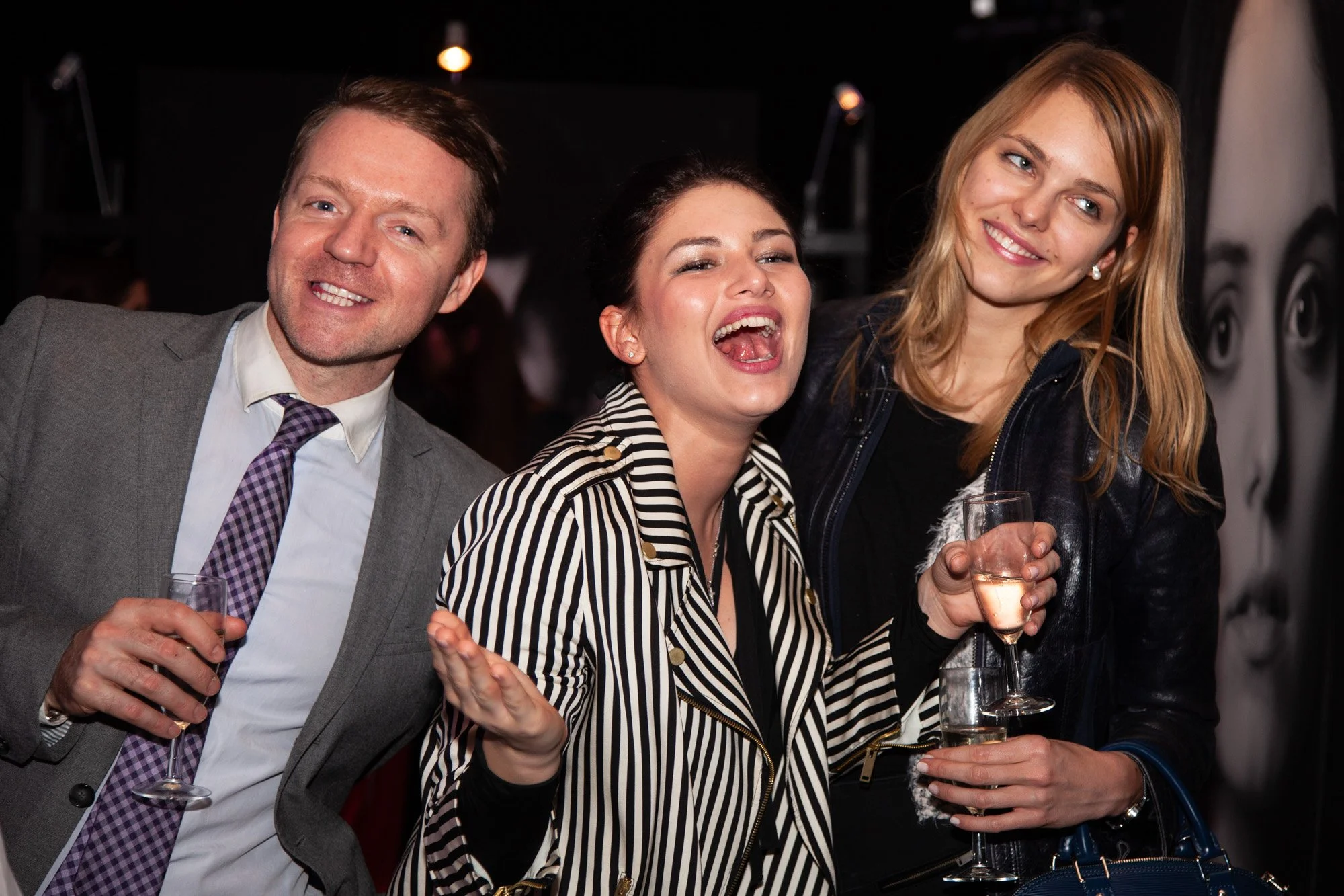 Three guests laughing together while holding drinks at an awards celebration.