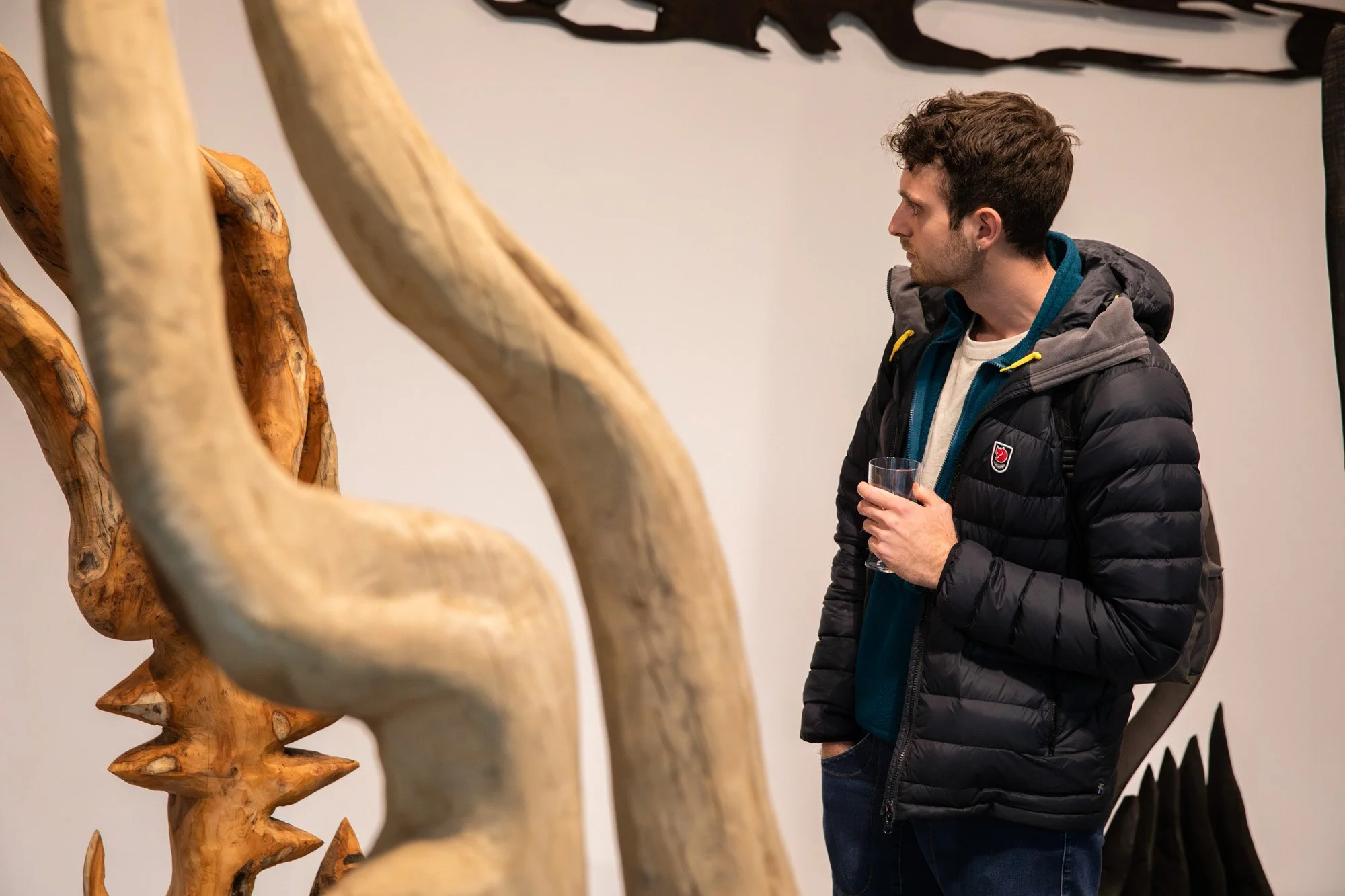 Visitors viewing tall wooden sculptures at a Sol Bailey Barker exhibition.