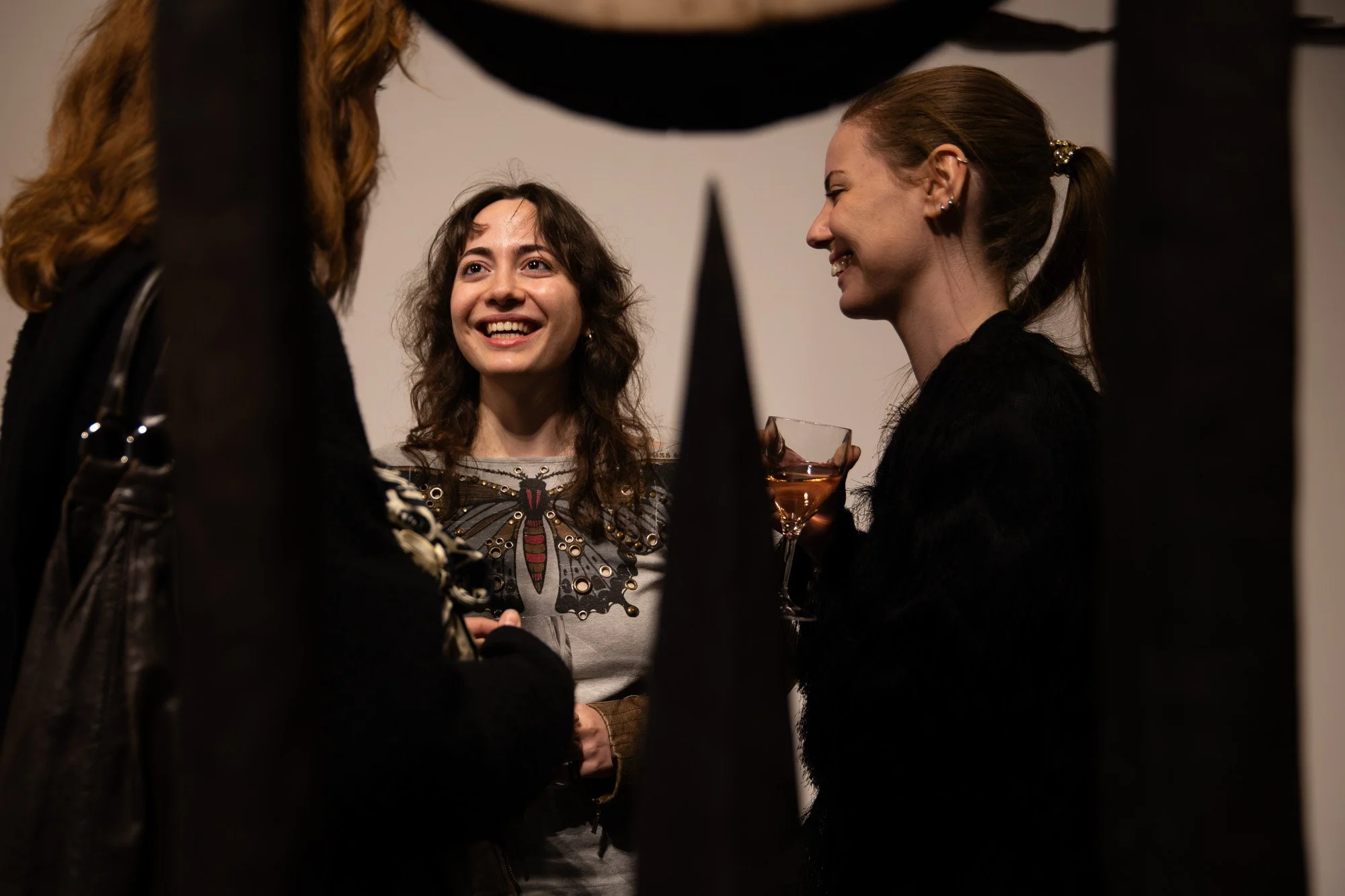 Guests smiling and chatting over drinks at a Sol Bailey Barker exhibition reception.