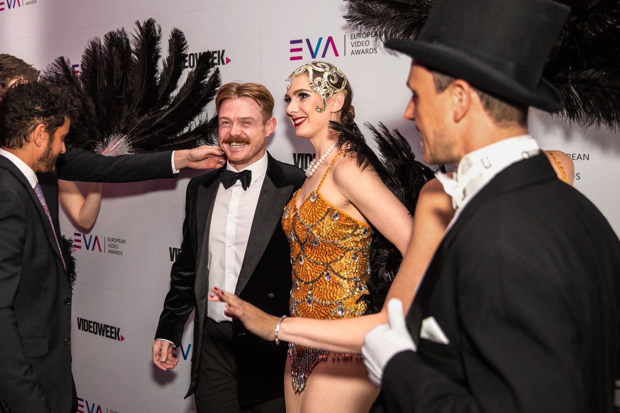 Guests posing with performers in feathered costumes at the European Video Awards.