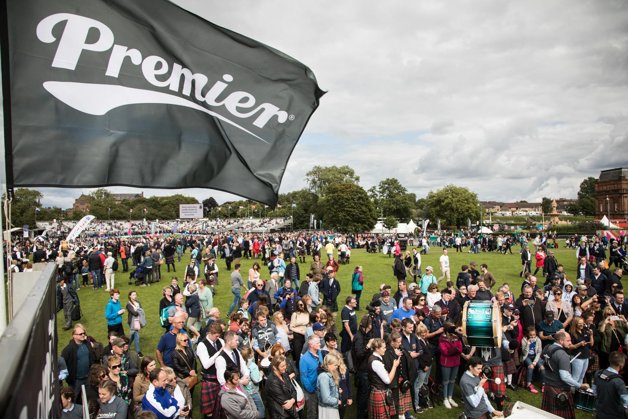 A large crowd gathered on a grassy field beneath a Premier banner at a pipe-band competition.