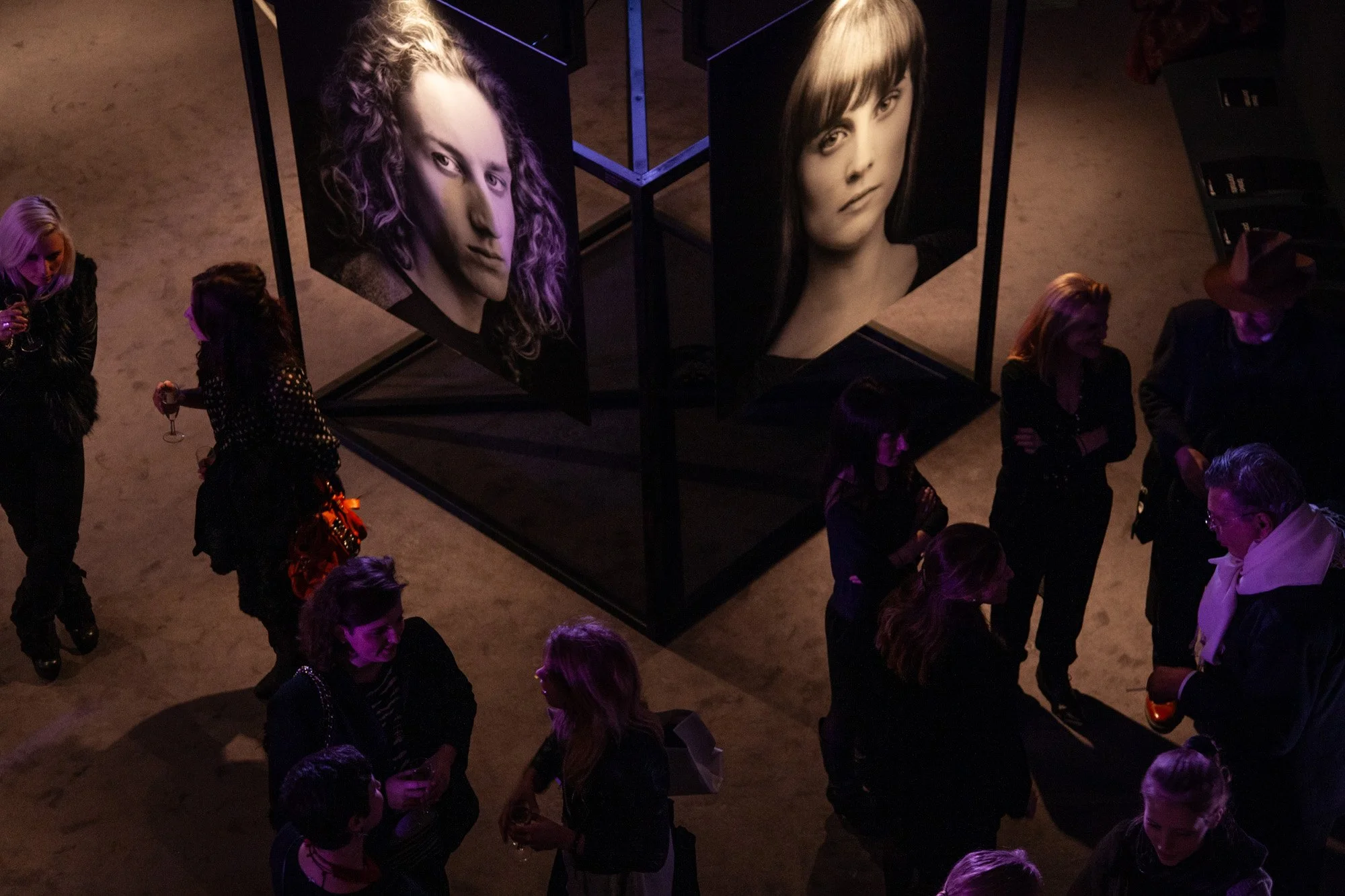 Guests mingling beneath large portrait photographs at an evening reception.