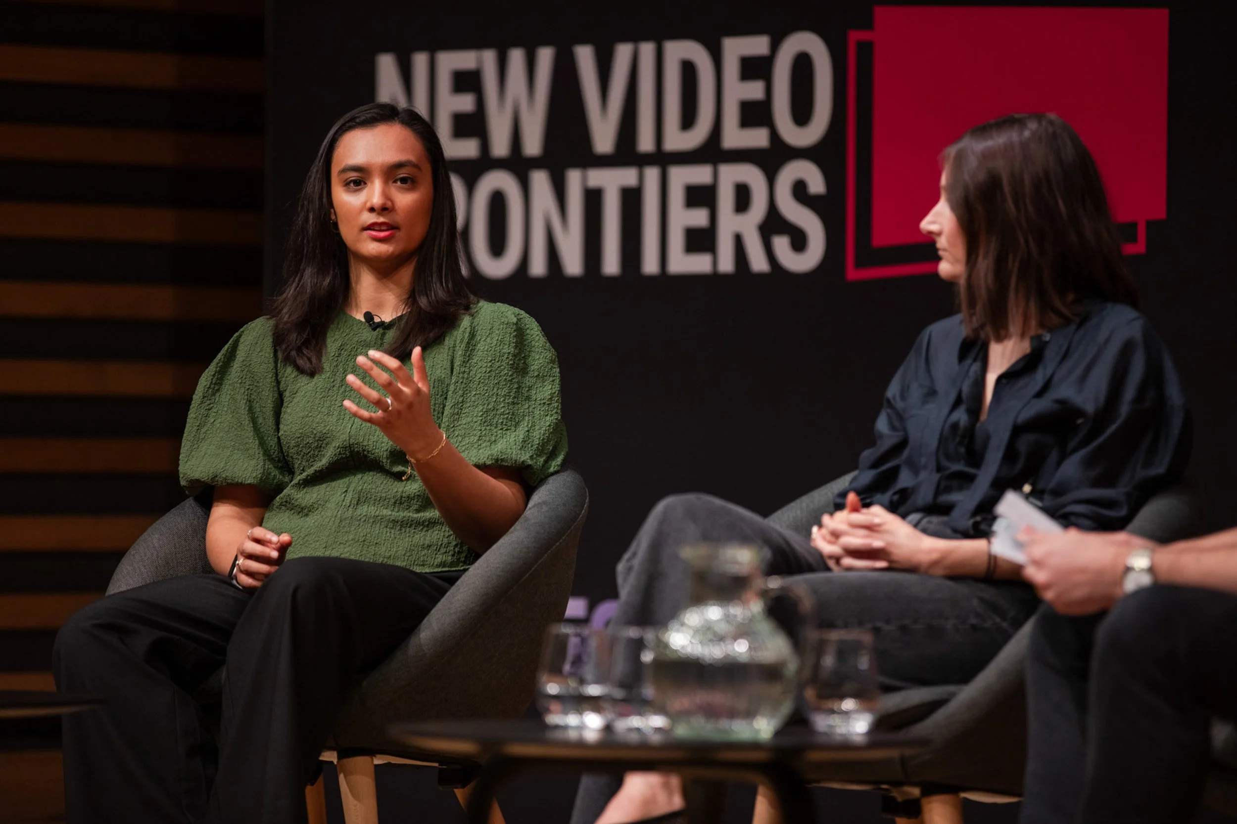 Woman in a green top speaking during a panel discussion at New Video Frontiers, with another speaker listening beside her.