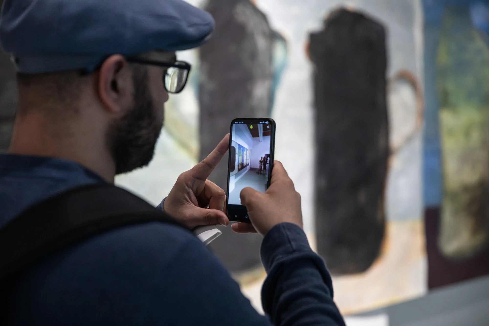 A visitor photographing an artwork with a smartphone at the Locus of Voices exhibition.