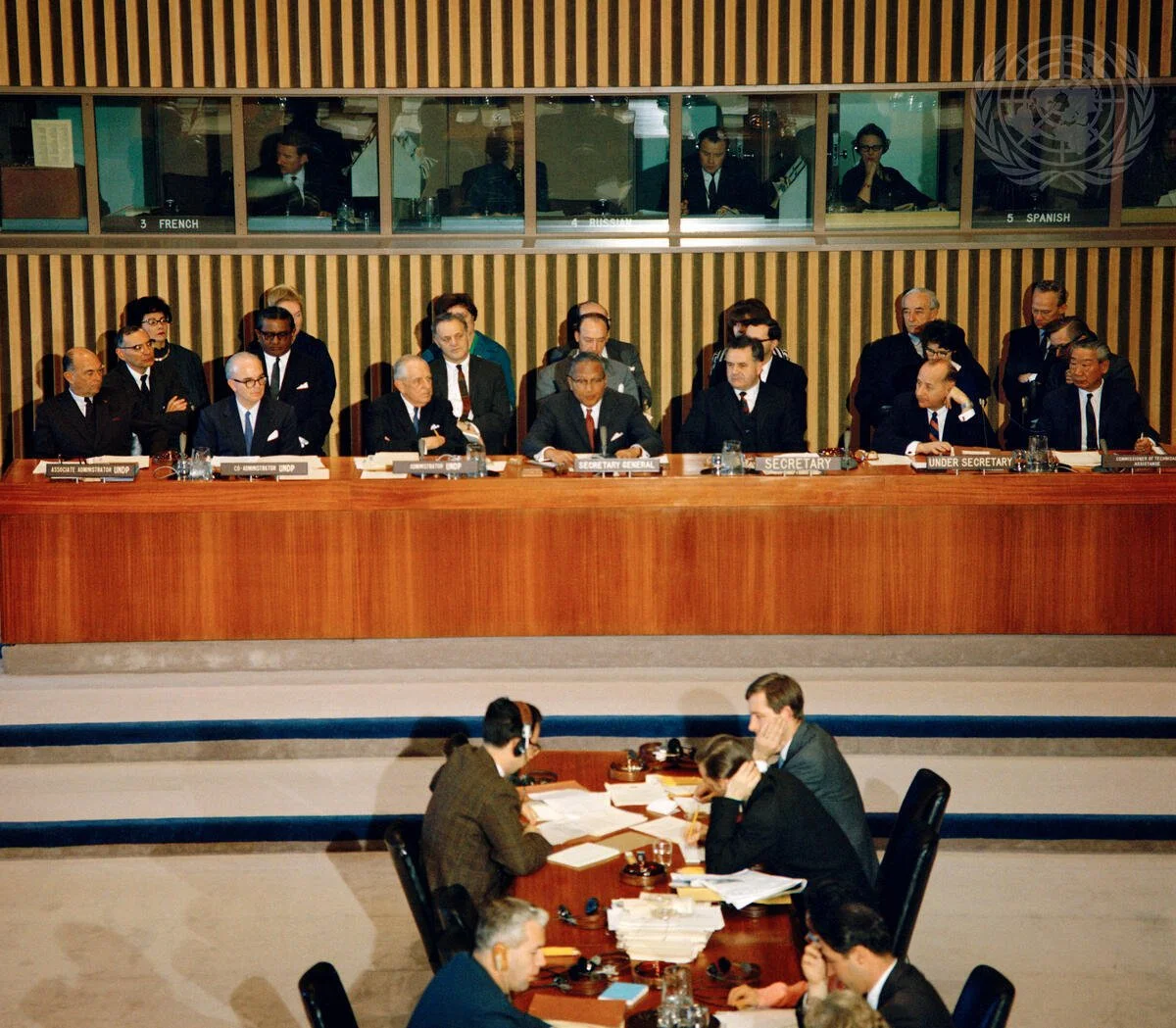 United Nations security council meeting with delegates seated at a long table, with nameplates indicating their roles, in a large conference room.