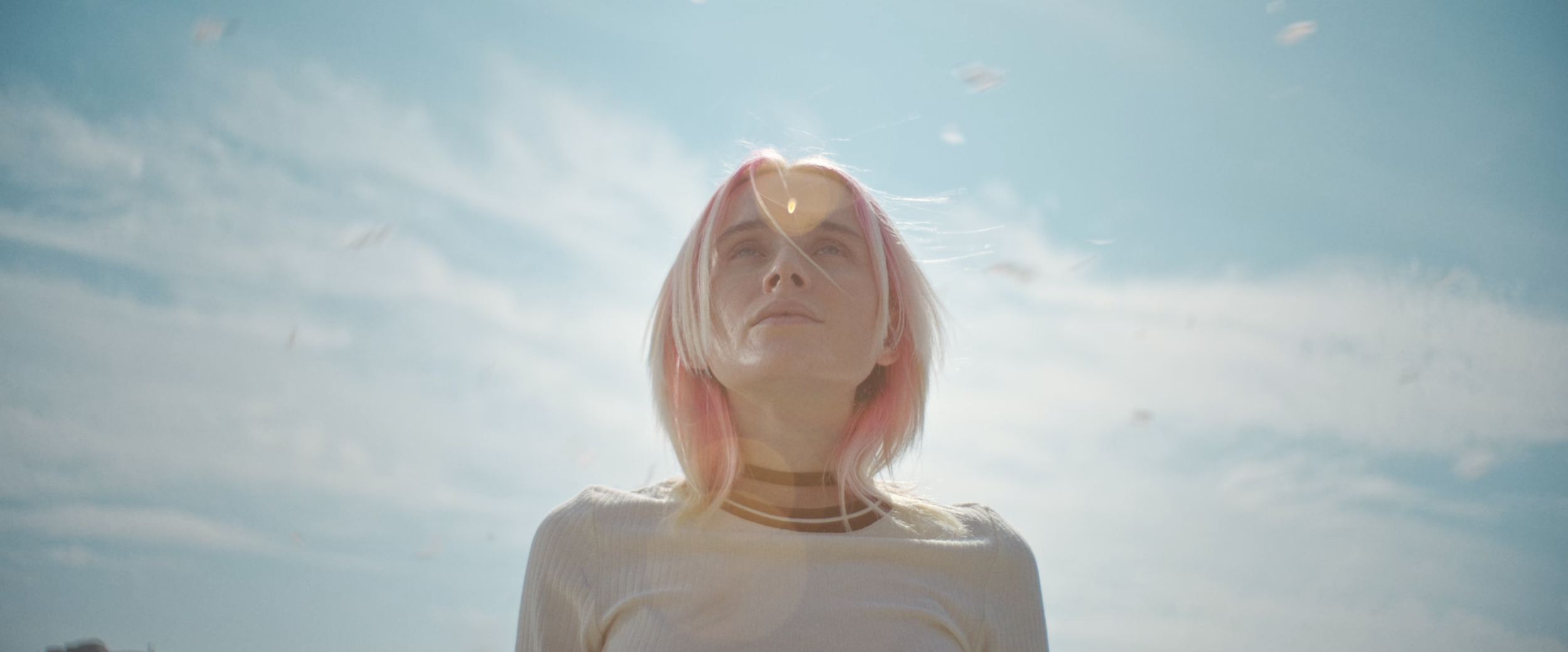 A woman with pink hair looking up at the sky on a sunny day.