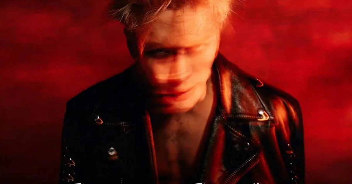 Blurry red-toned photo of a man with blonde hair wearing a black leather jacket, looking downward with a slight smile. Jackson Wang Magic Man Coachella Performance.