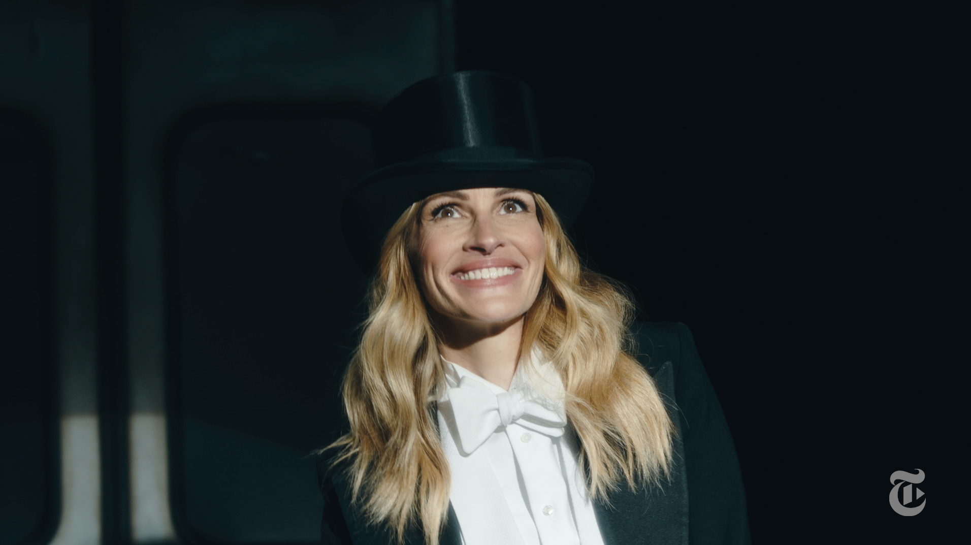 A woman with long blonde hair smiling, wearing a black top hat and a black tuxedo with a white shirt and bow tie. Julia Roberts photo by Philip Montgomery for New York Times Magazine