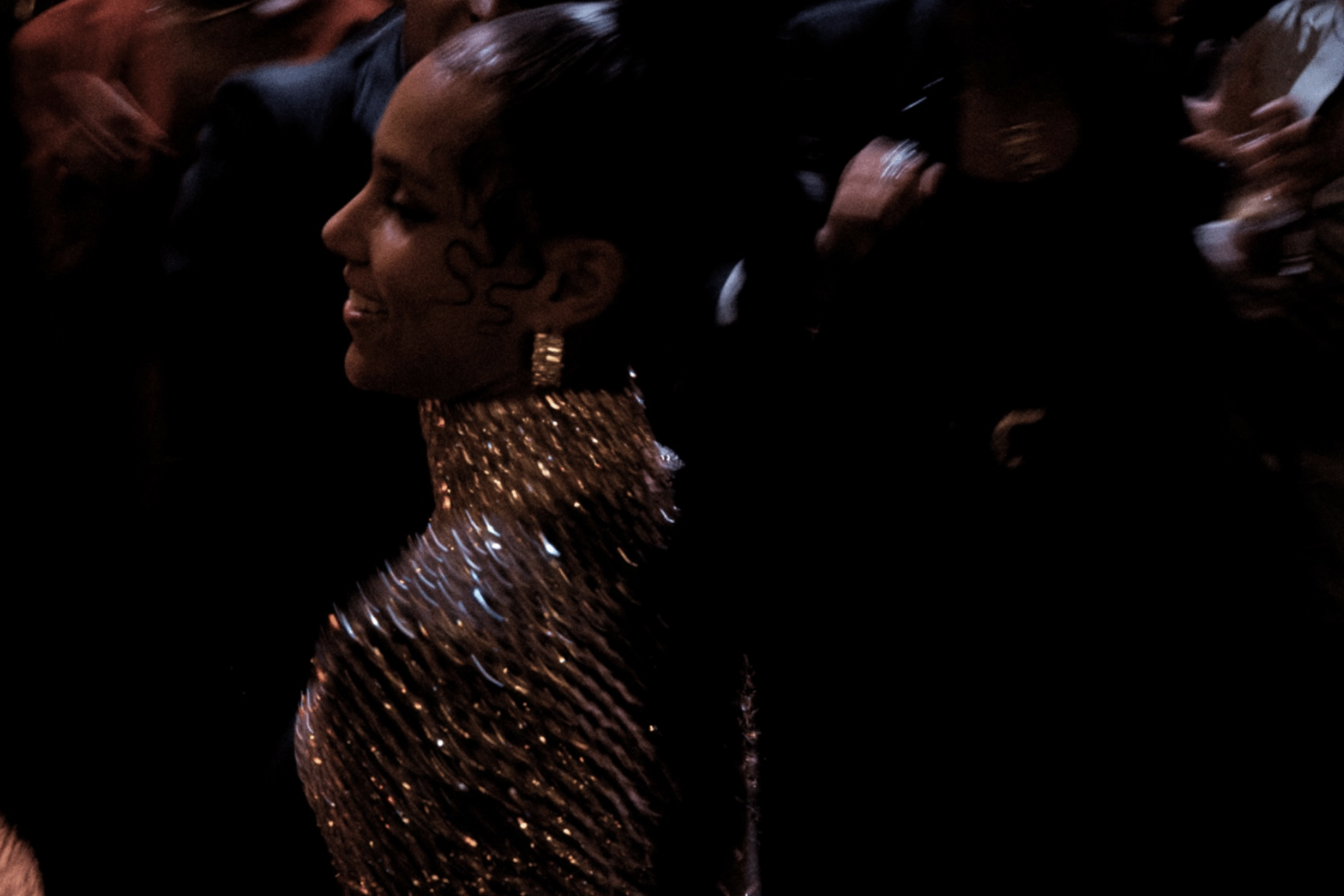 A woman with dark hair in an updo, wearing large earrings and a sparkling, metallic dress, smiling at an event.