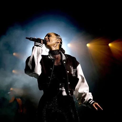 A female singer performing on stage with a microphone, wearing a black and white jacket, under colorful stage lights.