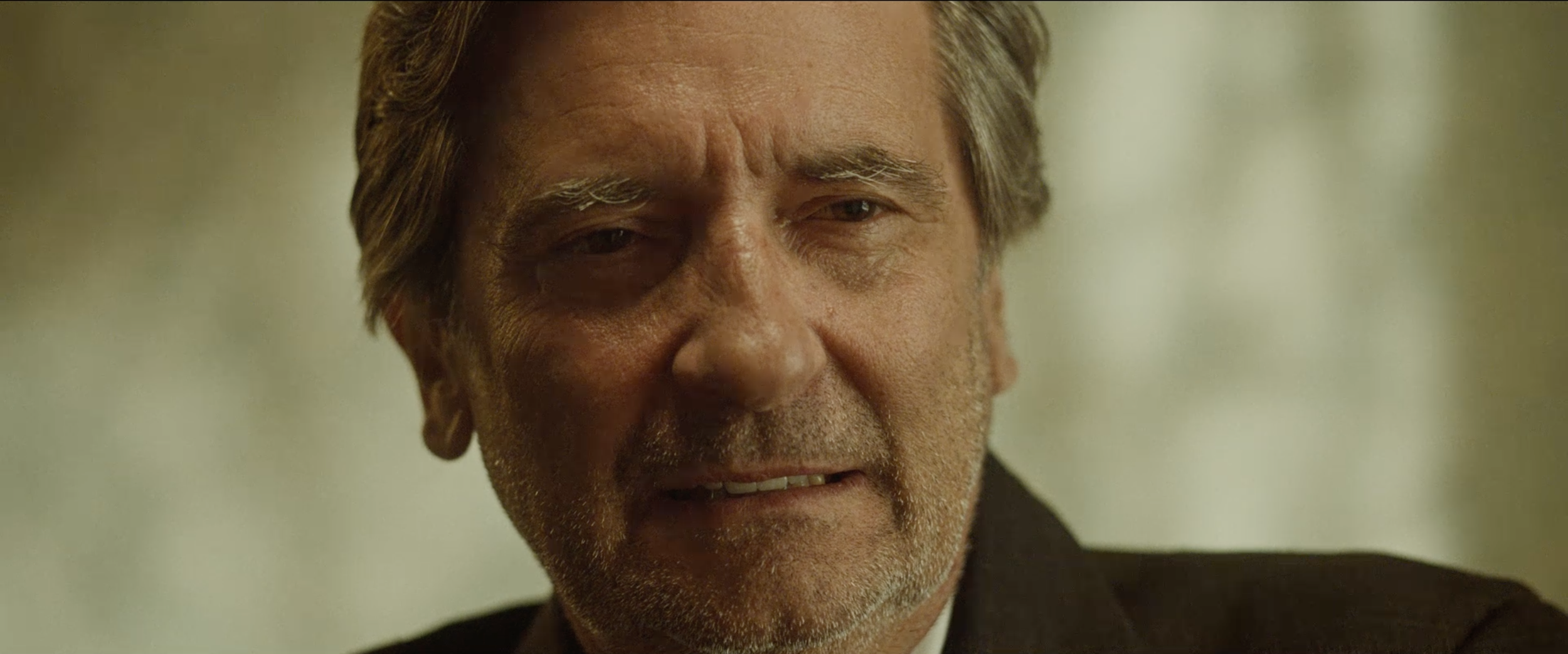 Close-up of an older man with gray hair and facial hair, showing an expression of concern or sadness.