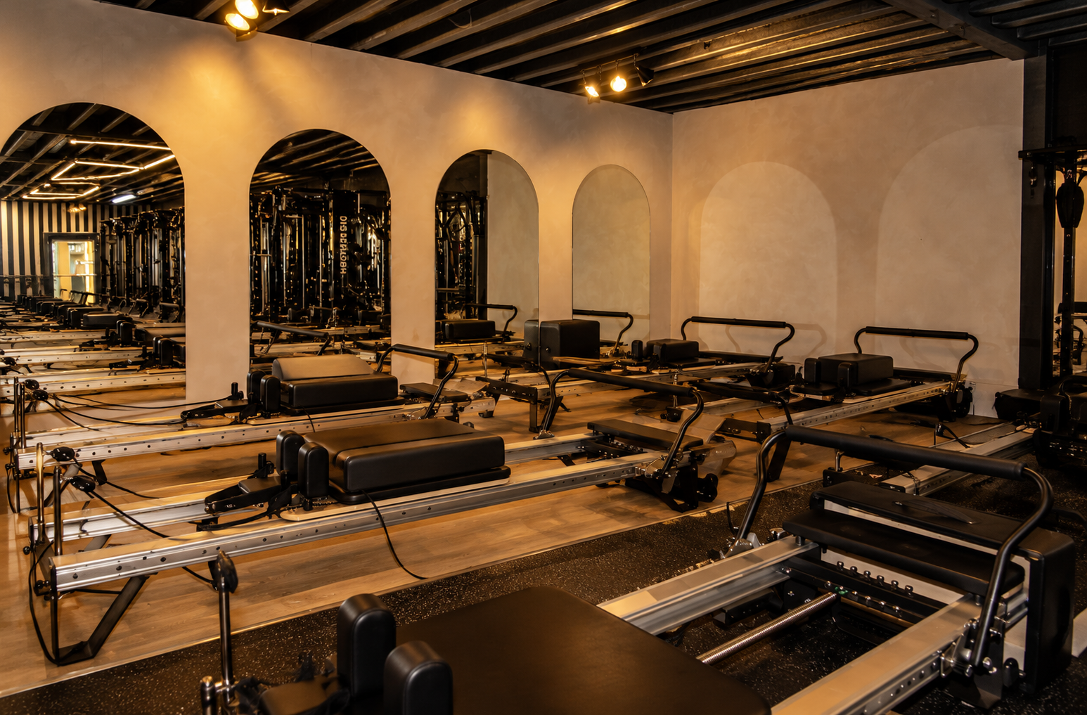Empty Pilates studio with reformer machines and mirrored wall.