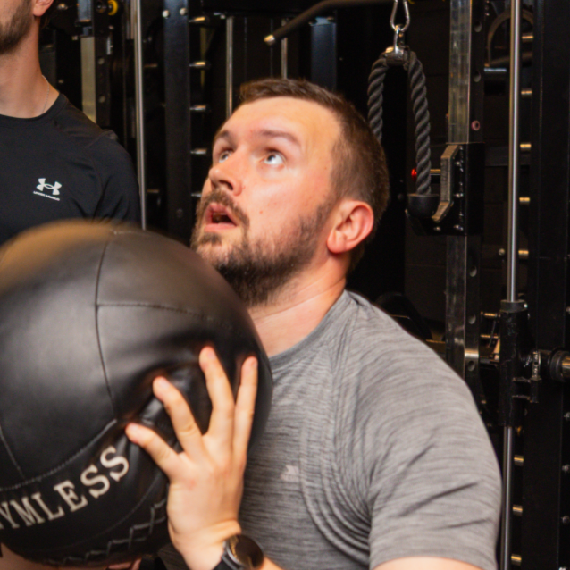 Man holding a medicine ball during a workout at a gym.