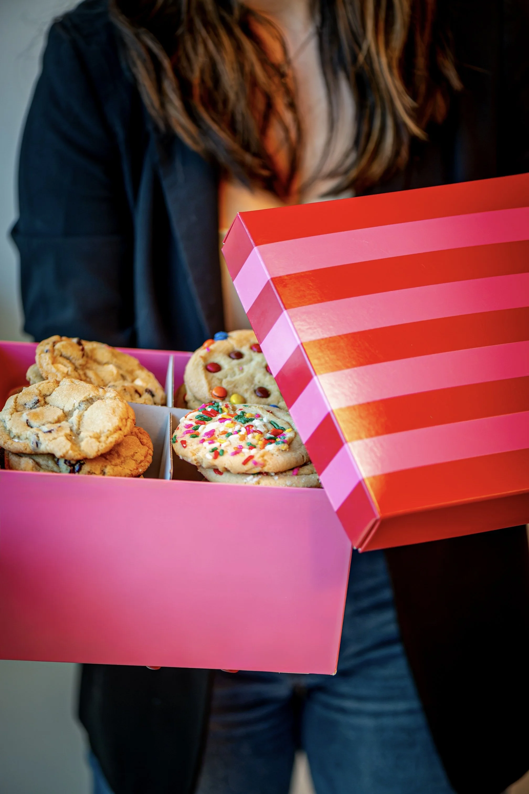 An open pink striped gift box filled with assorted cookies.
