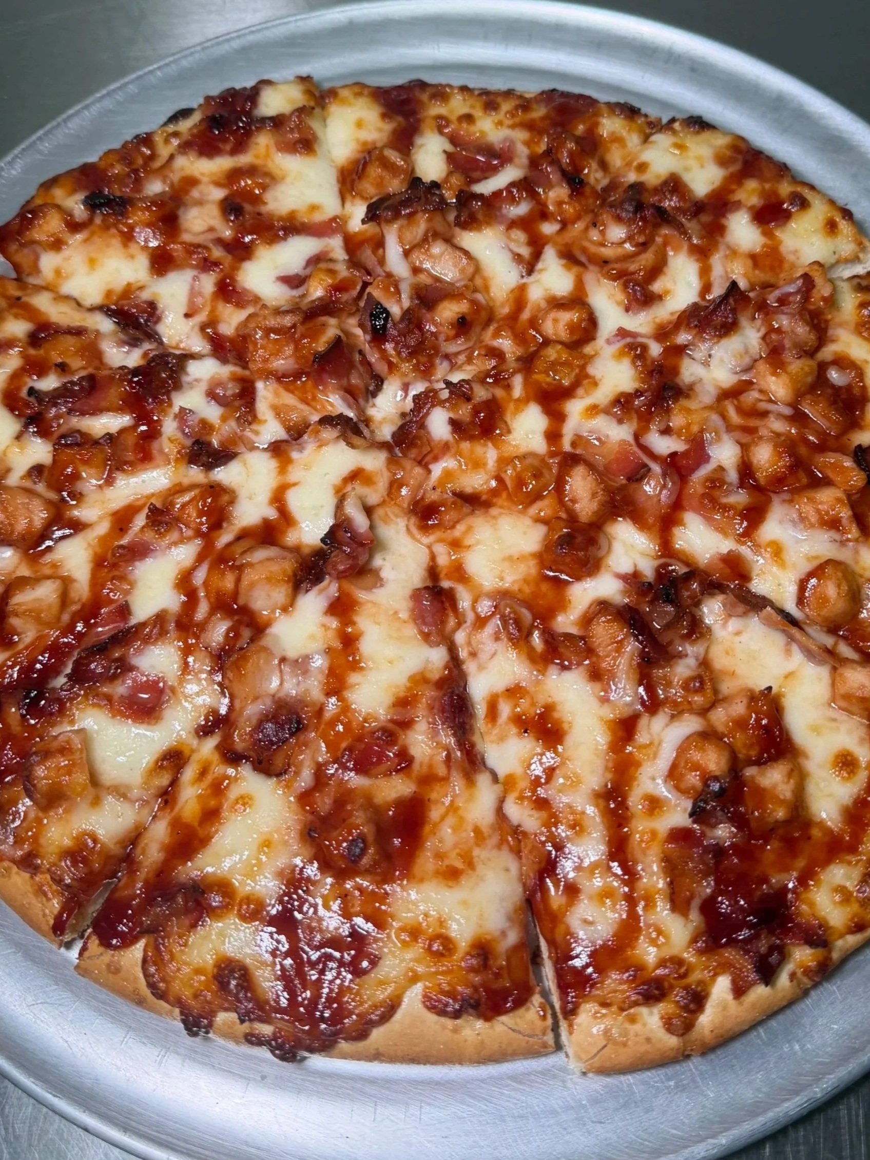 A whole pepperoni pizza with cheese and tomato sauce on a silver platter, with one slice cut out.