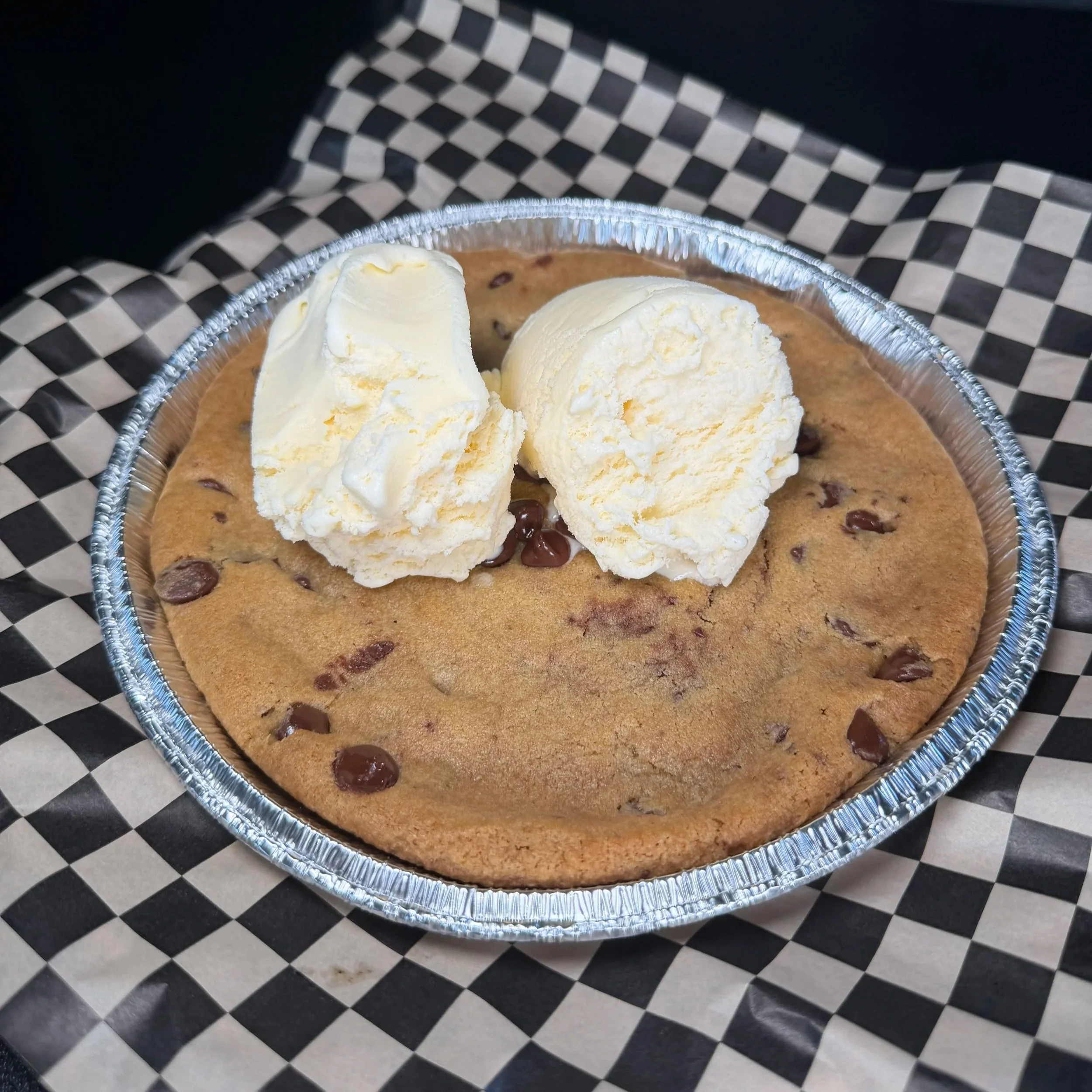 Chocolate chip cookie topped with two scoops of vanilla ice cream served in a disposable aluminum tray