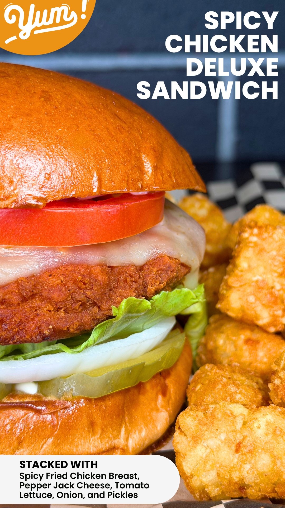 Close-up of a stacked spicy fried chicken sandwich with lettuce, pickles, tomato, pepper jack cheese, and a brioche bun, alongside crispy chicken tenders.