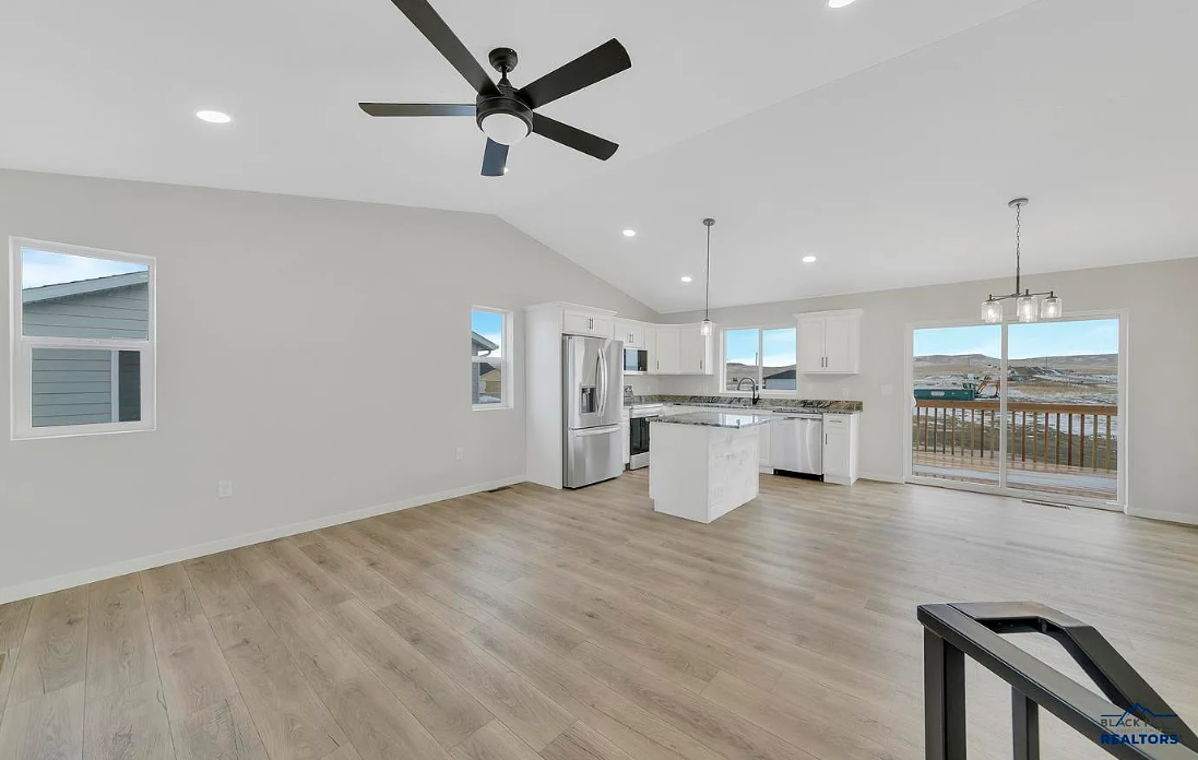 Open-concept living area and kitchen with white cabinets, stainless steel appliances, granite countertops, light wood flooring, ceiling fan, and sliding glass door leading to a balcony with outdoor view.