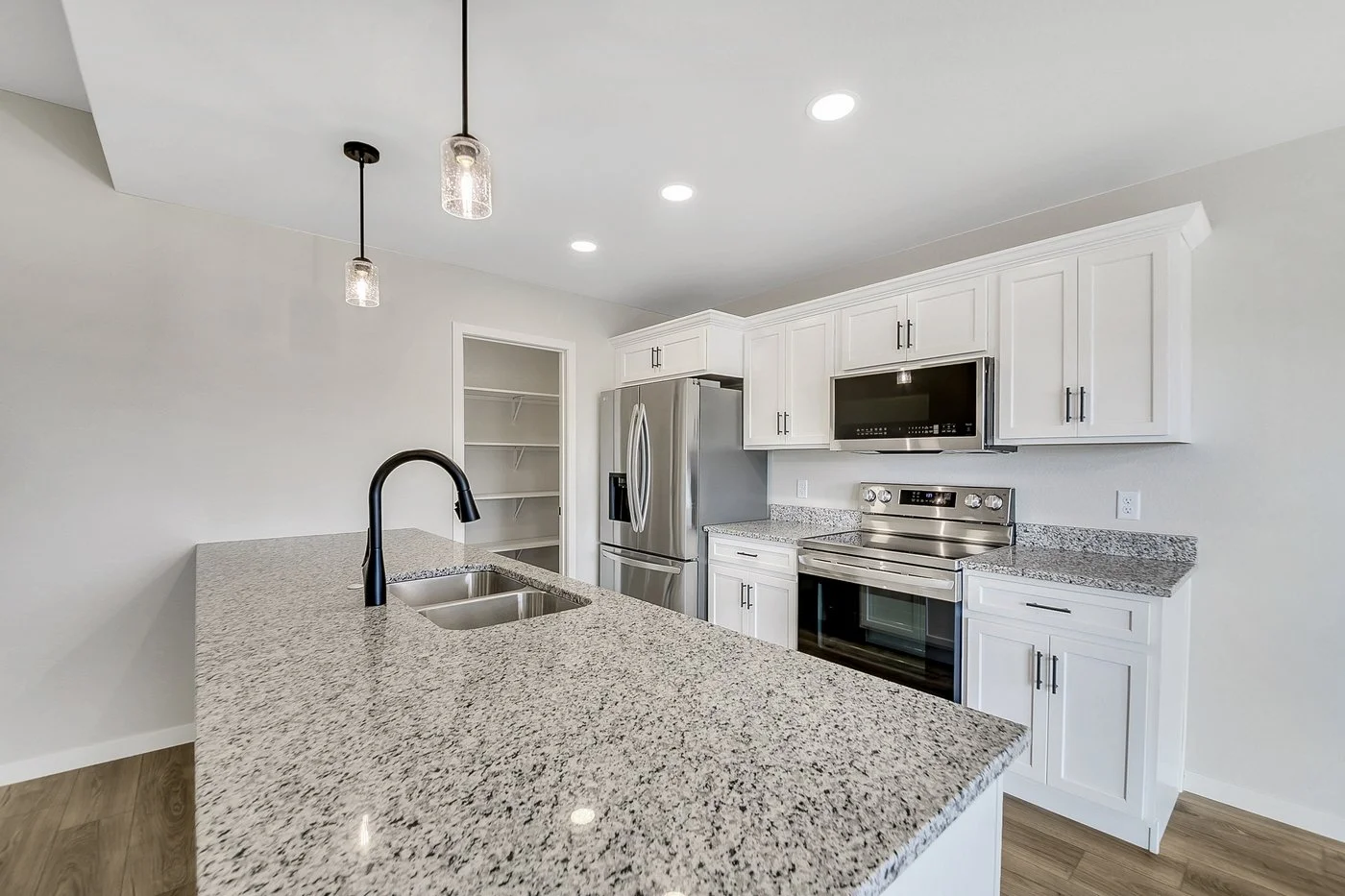 Modern kitchen with white cabinets, granite countertops, stainless steel appliances, and pendant and recessed lighting.