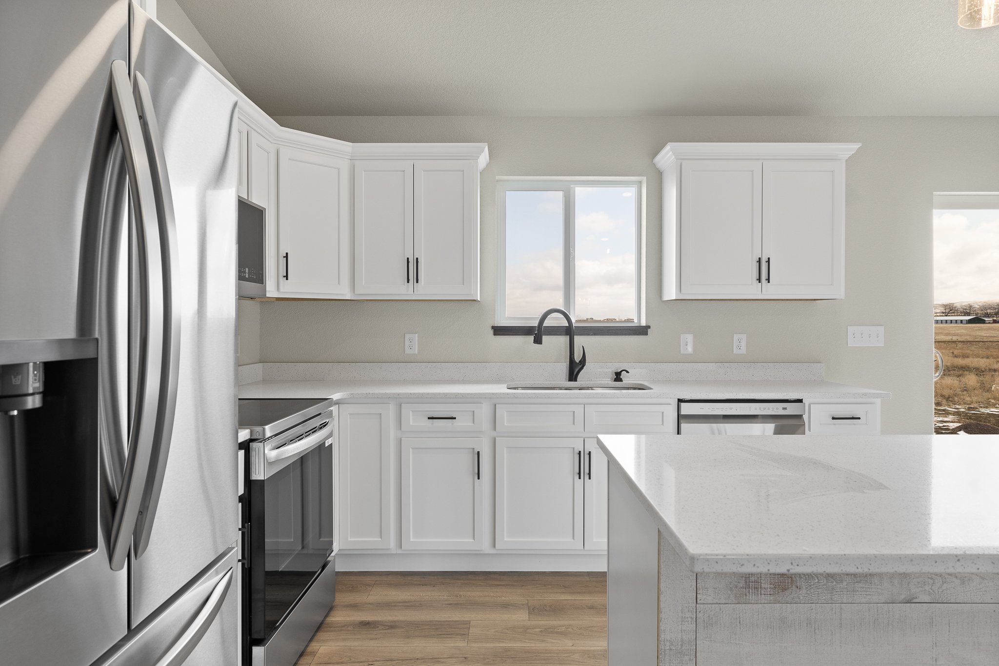 Modern kitchen with white cabinets, stainless steel appliances, a large window, and wood flooring.