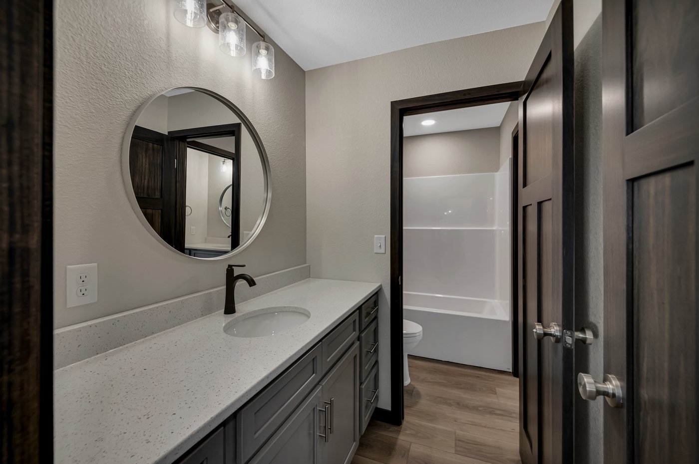 Bathroom with a vanity, round mirror, and a separate shower and tub area.
