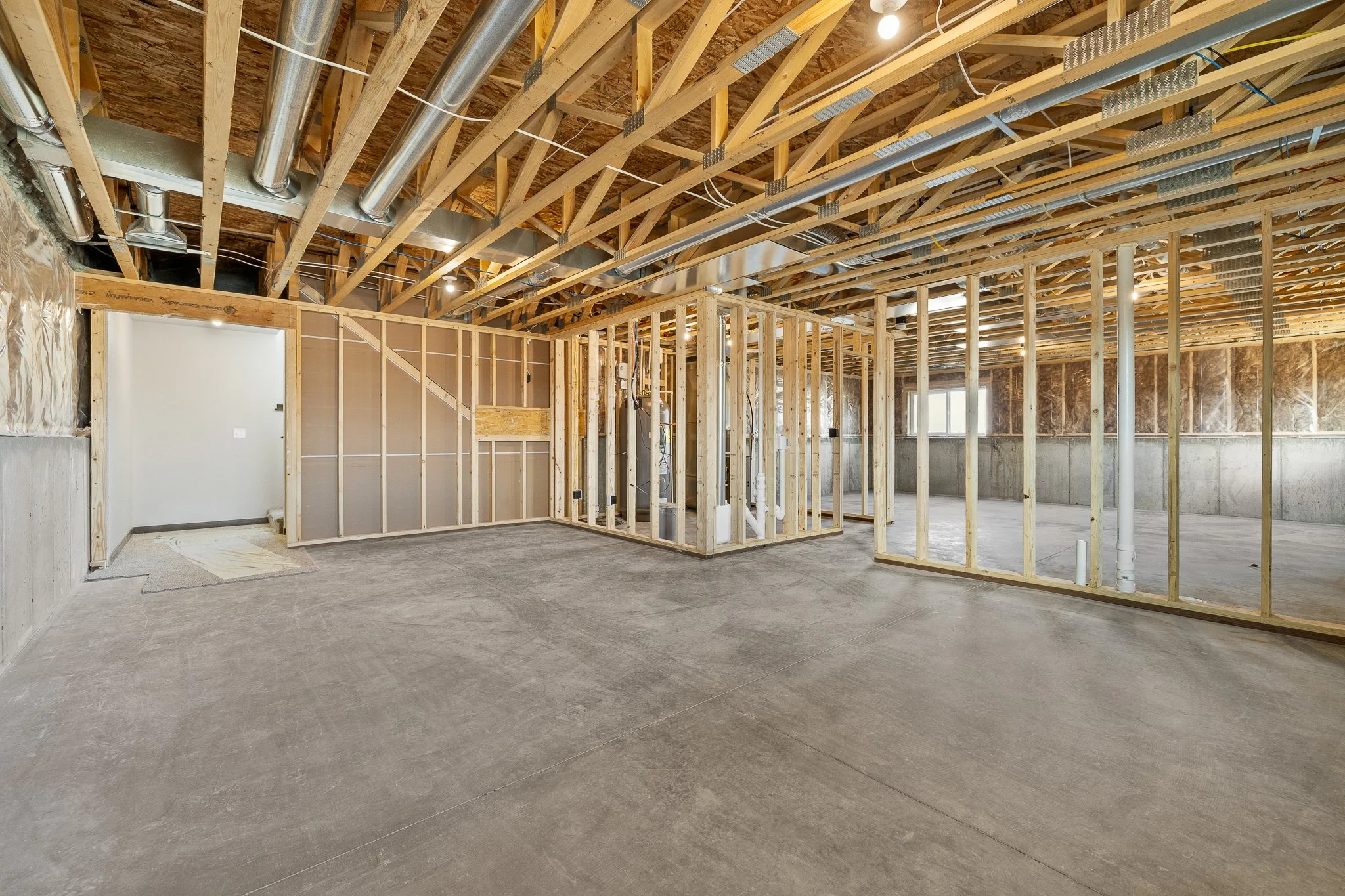 Interior view of a building under construction, showing exposed wooden framing, ductwork, and a concrete foundation with some drywall installed.