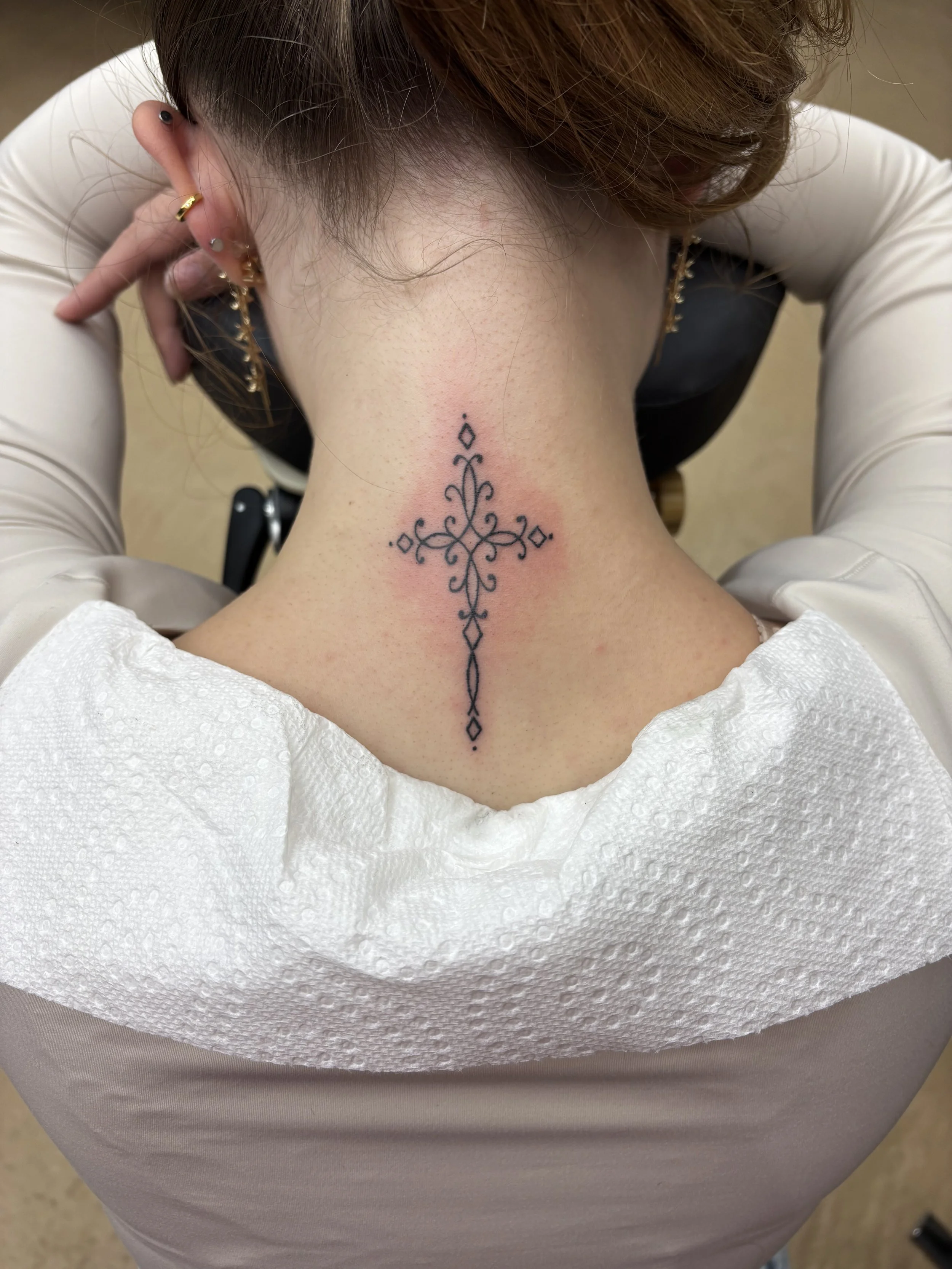 Fine line ornate cross tattoo on the back of a womans neck by Altered Tattoo Co