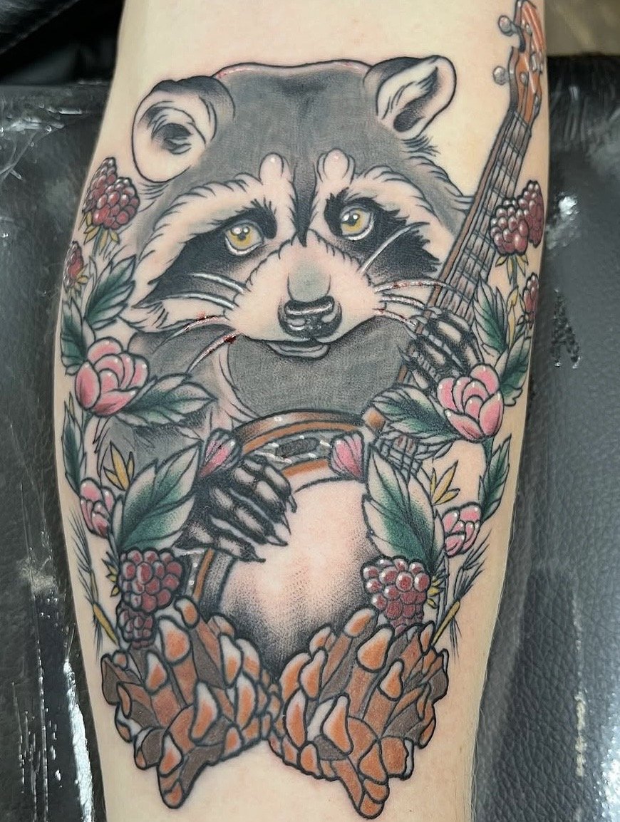 Neo traditional racoon playing a banjo tattoo on a forearm by Altered Tattoo Co