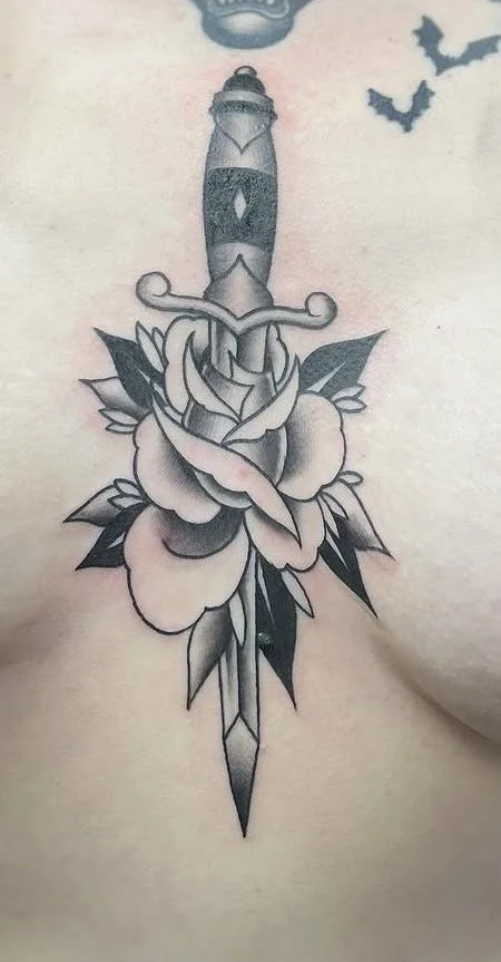 Black and grey American Traditional dagger through a rose tattoo on a sternum by Altered Tattoo Co
