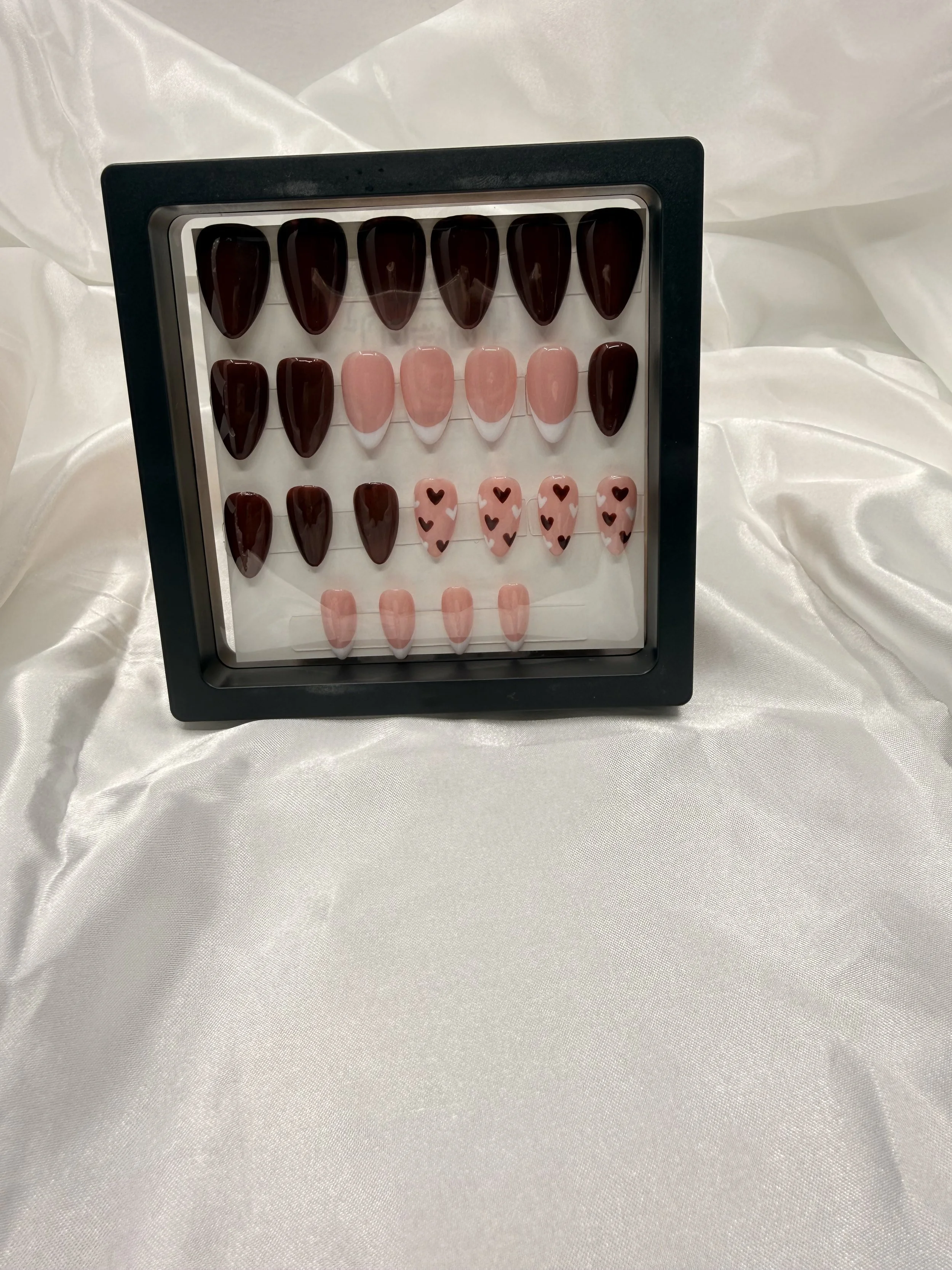 Glossy chocolate brown almond-shaped press-on nails with pink French tips and black heart designs.