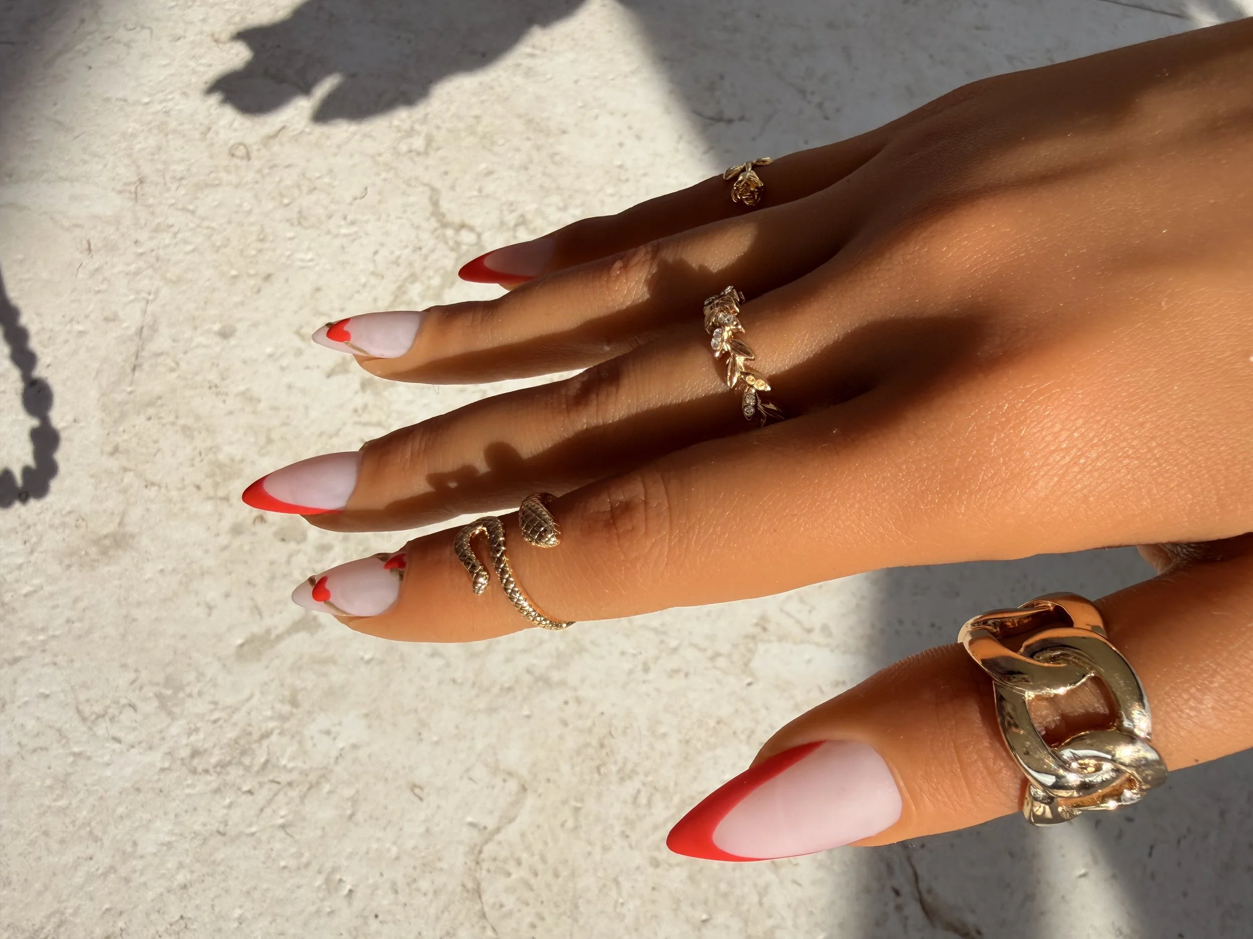side view Matte stiletto press-on nails with nude pink bases, red V-shaped French tips, and delicate red heart designs.
