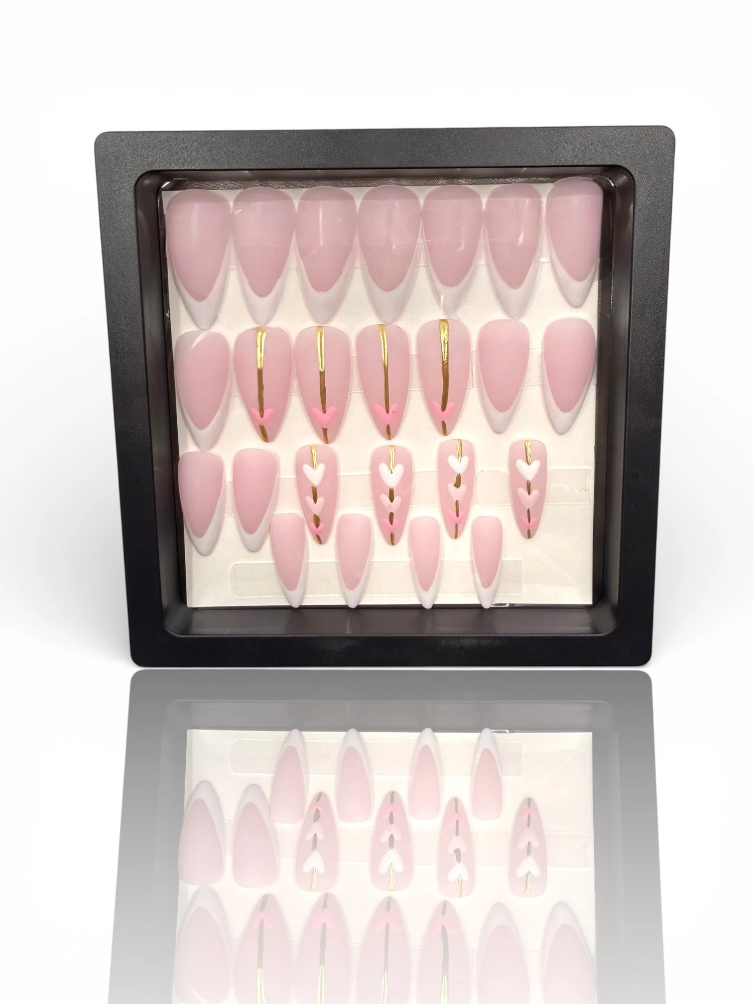 long matte Pink stiletto press-on nails with nude pink bases, French tips, gold accents, and delicate white heart designs.