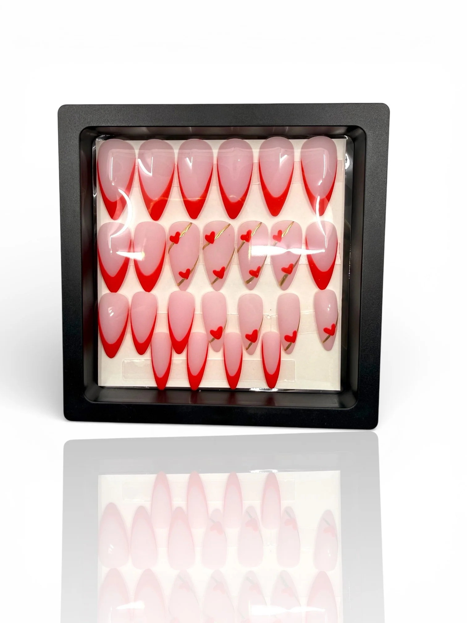 long Matte stiletto press-on nails with nude pink bases, red V-shaped French tips, and delicate red heart designs.