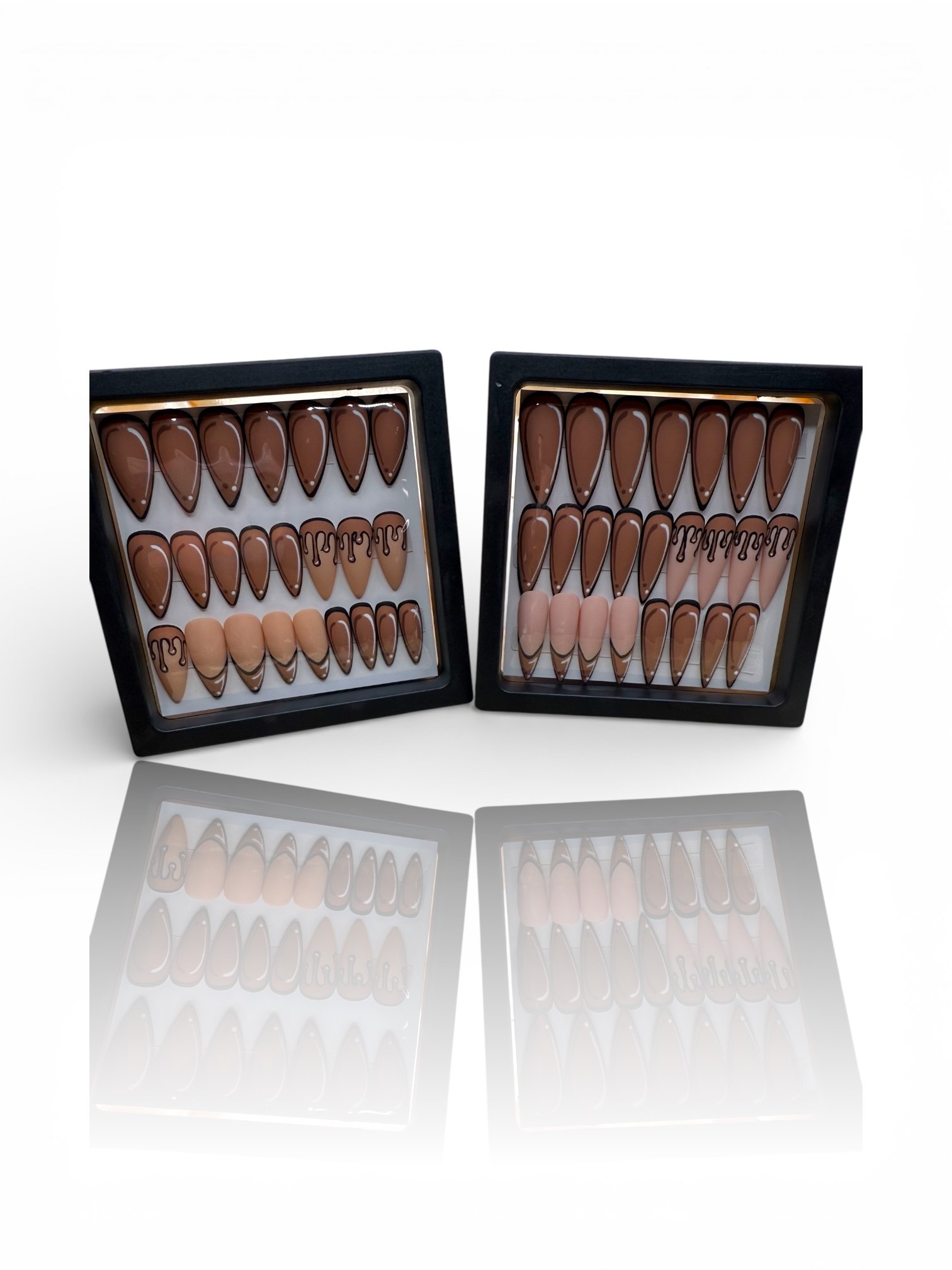 Brown almond press-on nails with black outline French tips, nude accent nails, and black drip nail art displayed in a black case. stiletto