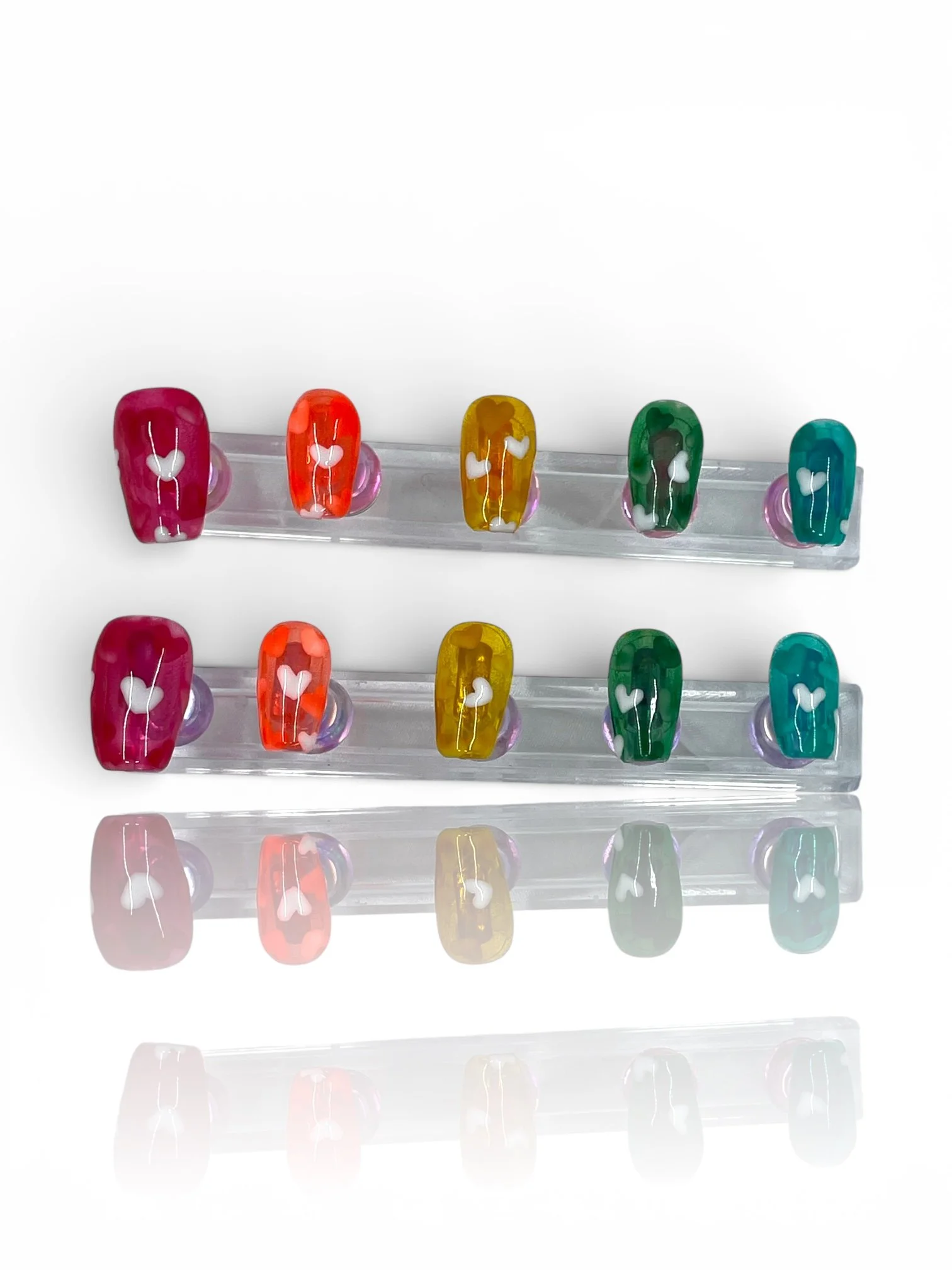 Glossy rainbow jelly square press-on nails in pink, red, amber, and green with translucent finishes and white heart designs.